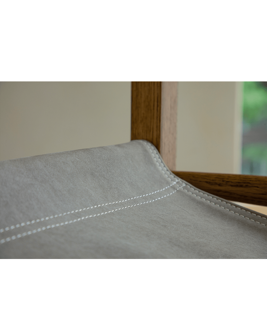 Safari Chair detail: Light gray fabric seat with white stitching, US Red Oak frame, and elegant design