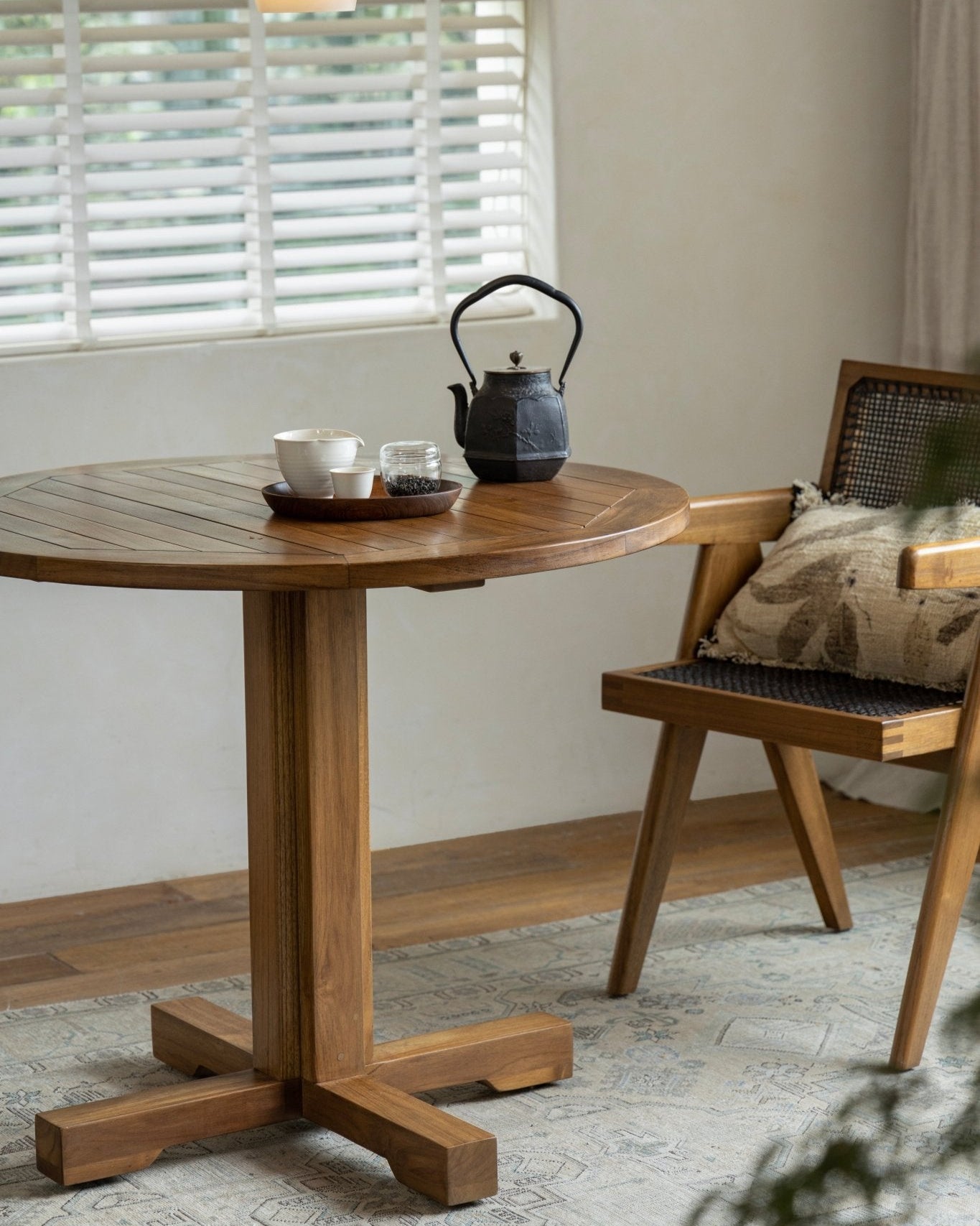 Ruby Teak Round Table in a cozy setting. Solid wood table with a black teapot, wooden chair, perfect for leisure.
