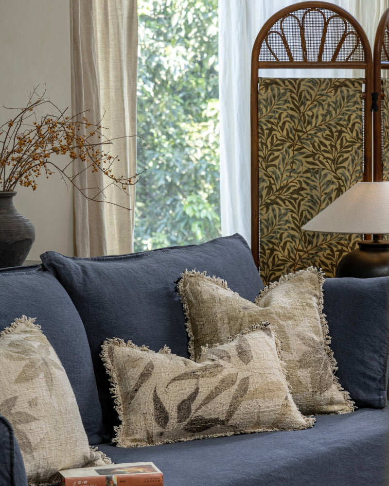 Verda pillow with natural plant motifs on a blue sofa, featuring a textured weave and frayed edges.