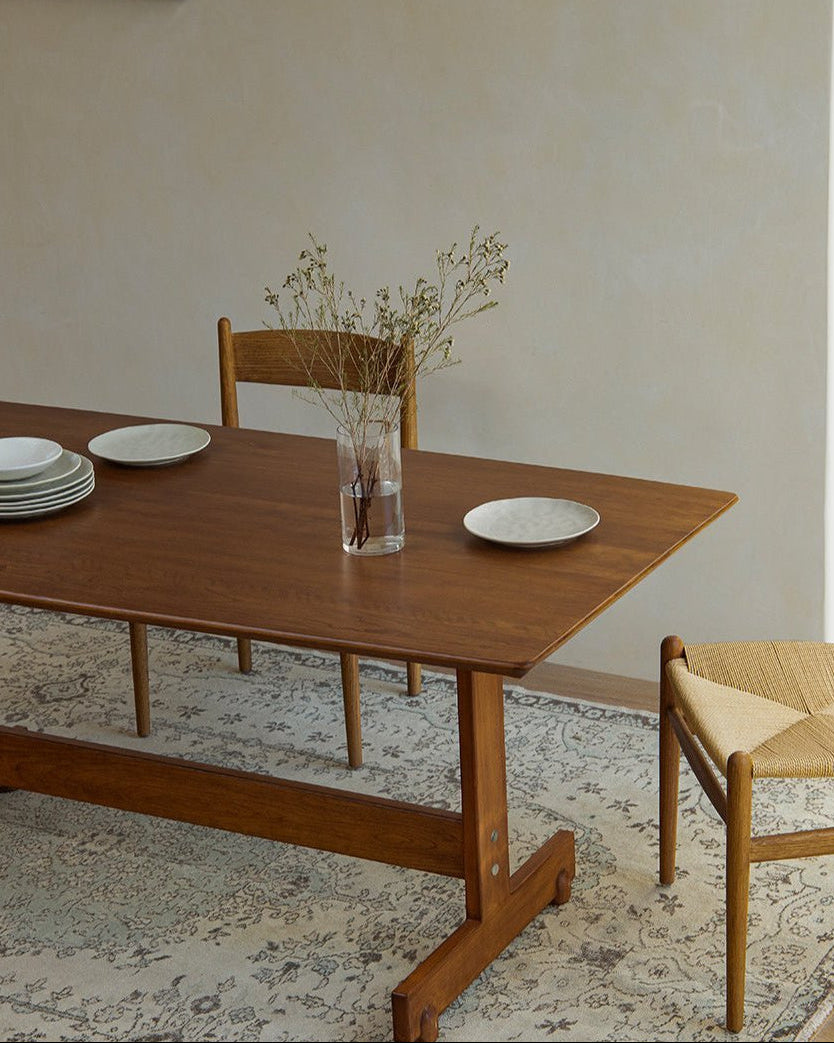 Hoof Dining Table solid wood with I-shaped base, set in a cozy dining setting with plates and chairs on rug
