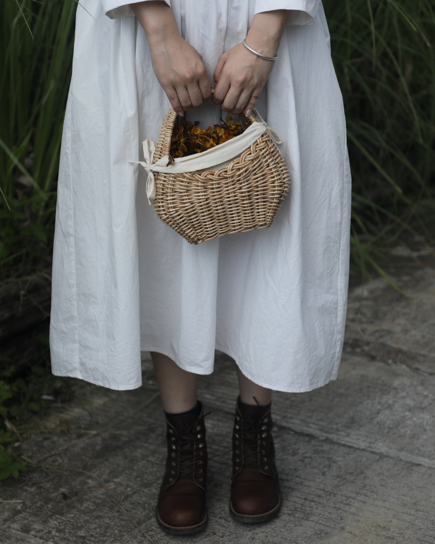 Nora Clutch small woven rattan basket with cotton lining, ribbon ties, and dried flowers.