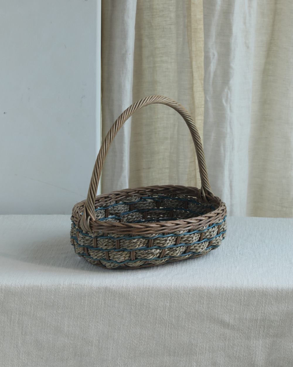Viney Tote Basket of woven natural and green rattan with blue accents and handle.