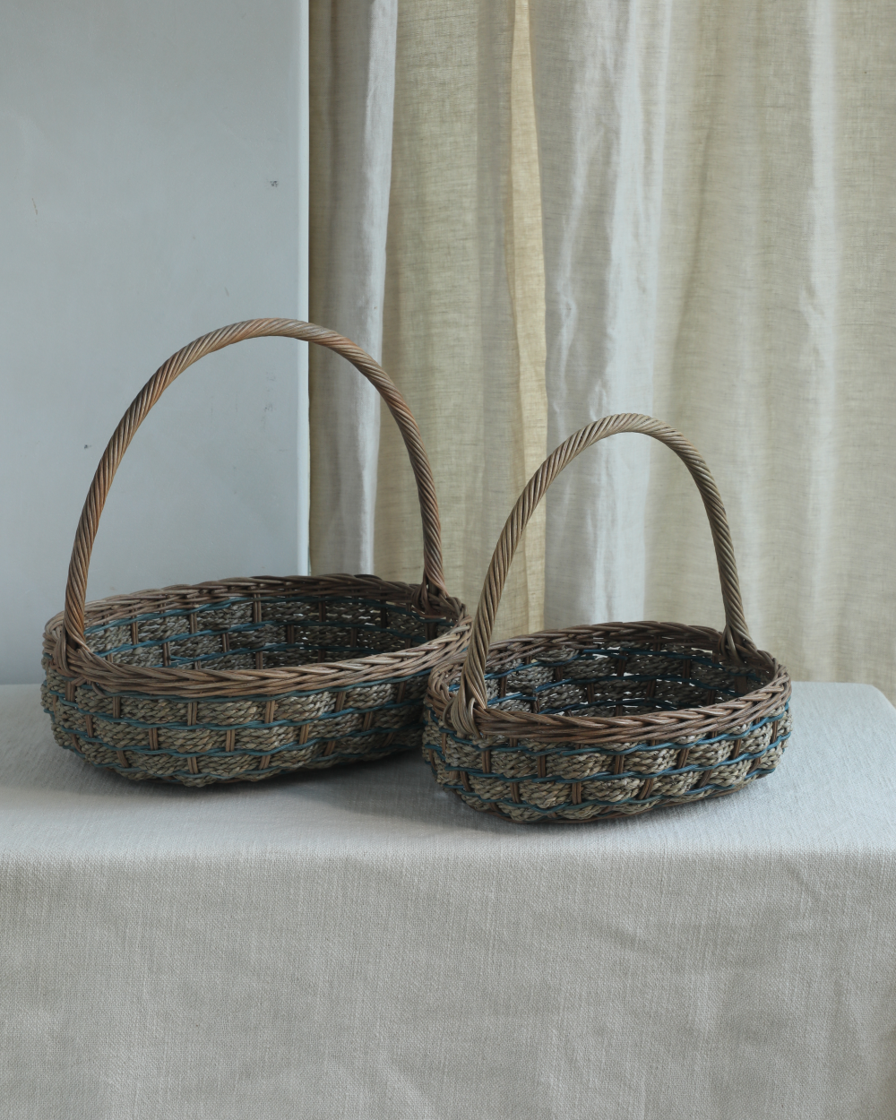Small and large woven rattan tote baskets with blue viney pattern and handles.