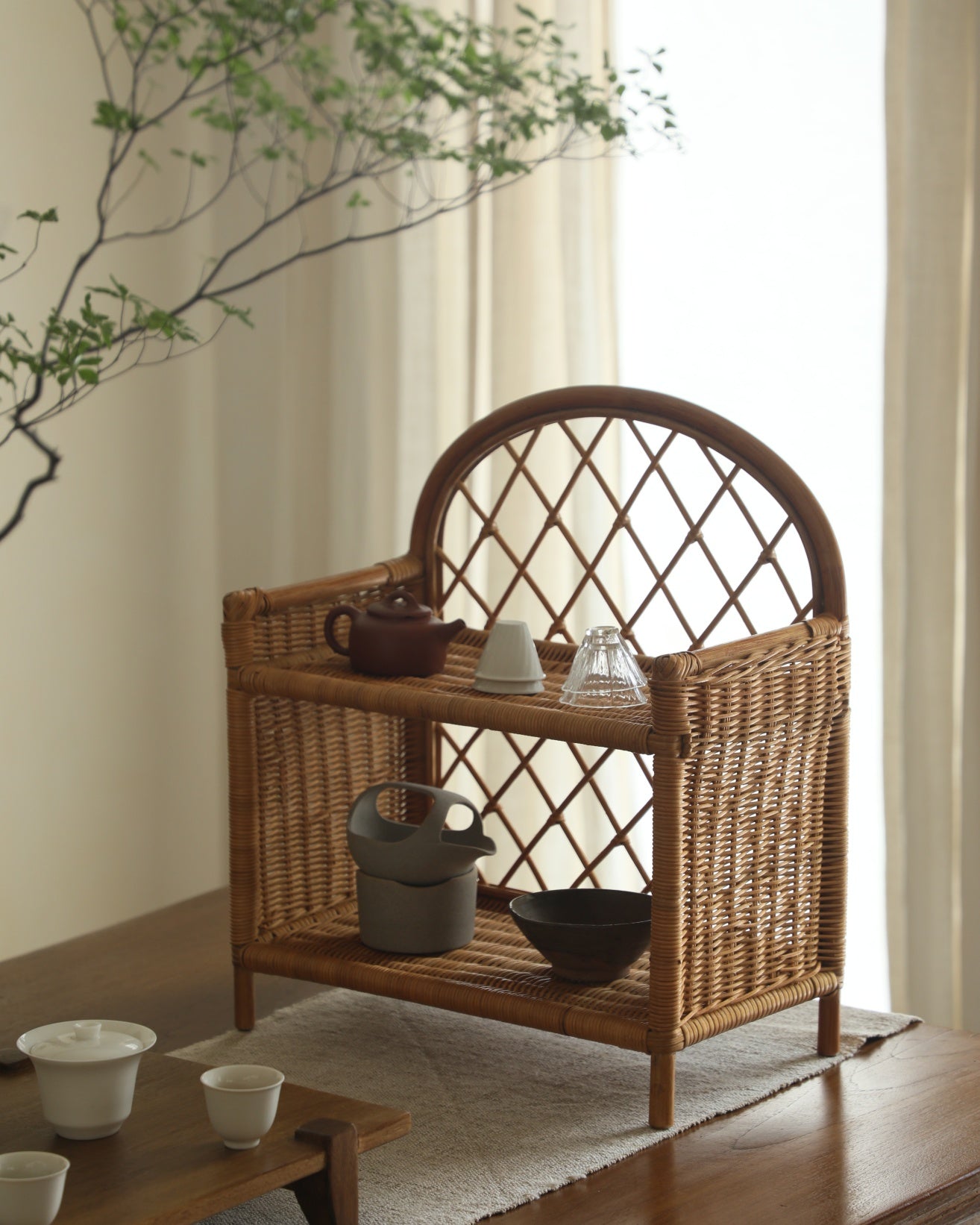 Solana Stand: Woven rattan with arched back and open shelves, displaying tea set.