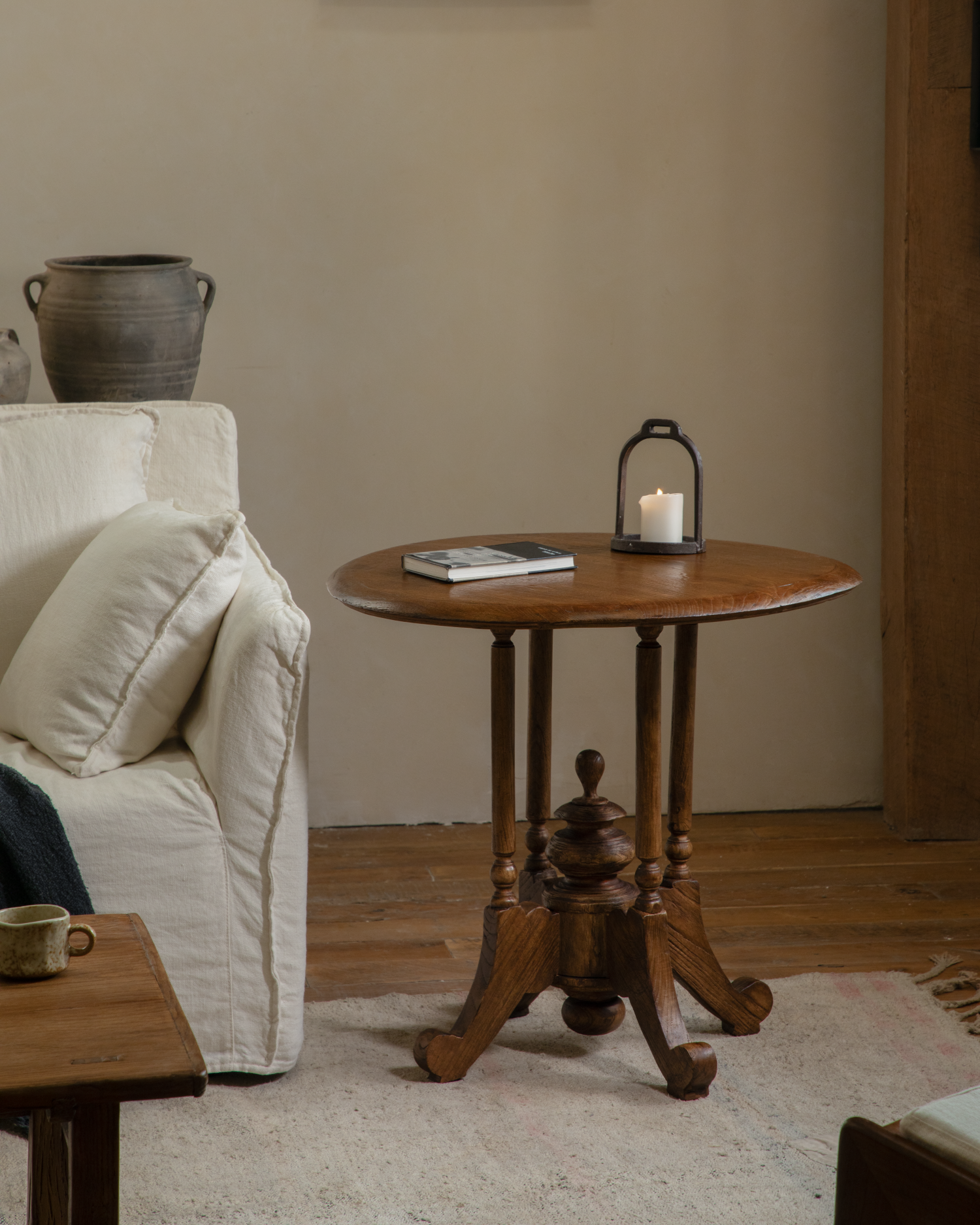 Vintage Indonesian teak wood round table with intricately carved base, lit candle lantern.