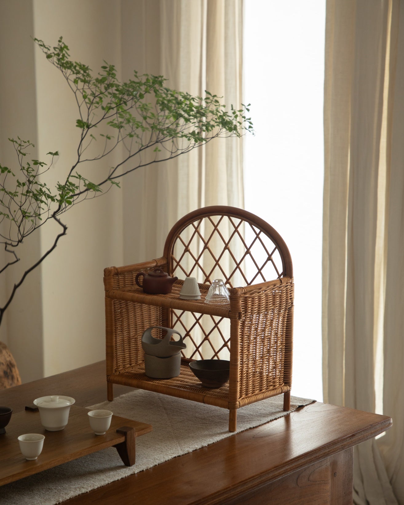 Solana Stand: Woven rattan two-tier shelf with arched back and open shelves, holding tea set.