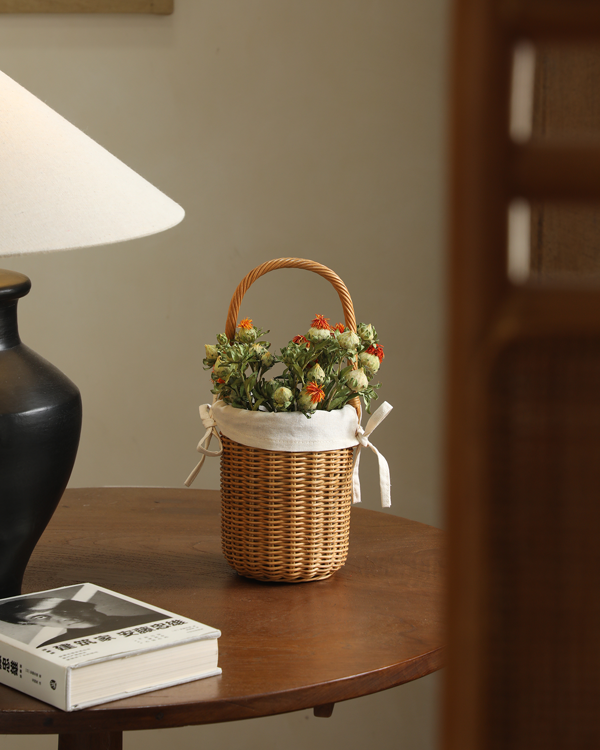 Natural hand-woven rattan Iris Basket featuring cotton lining and arched handle, filled with dried floral stems.