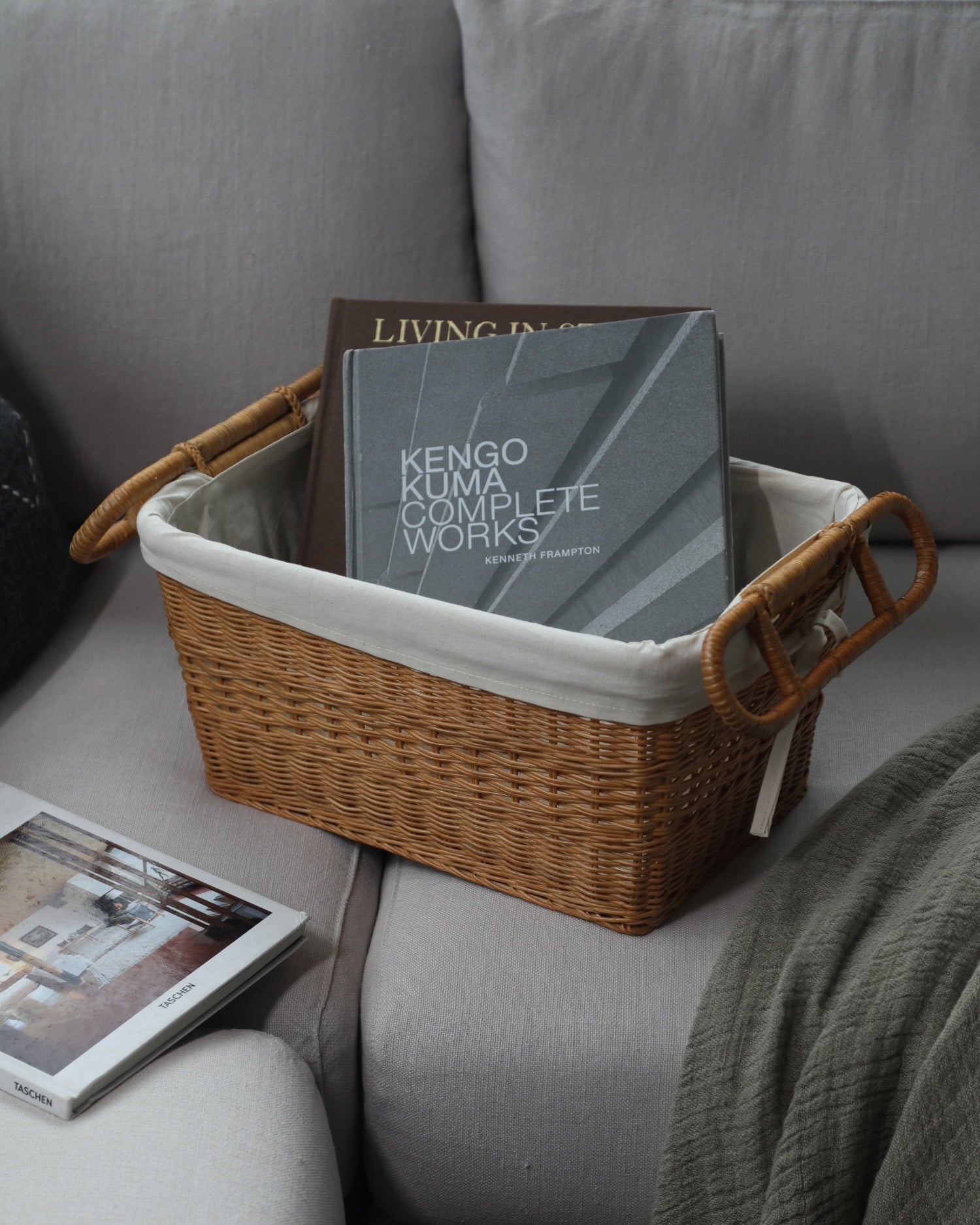 Hilda storage basket made of handwoven rattan with white cotton lining, featuring two carrying handles and filled with books.