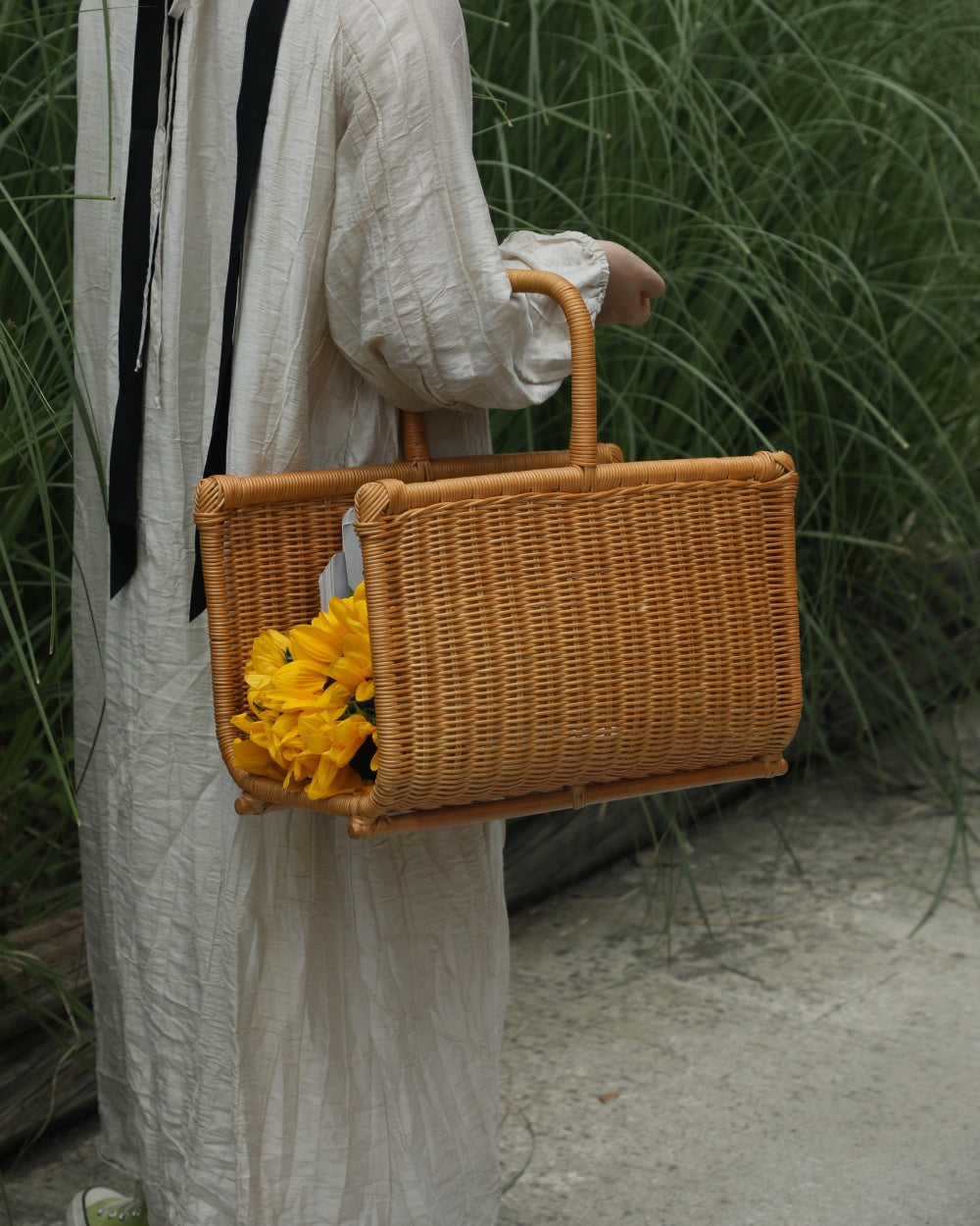 Folio Caddy woven book organizer with integrated handles, holding yellow flowers.