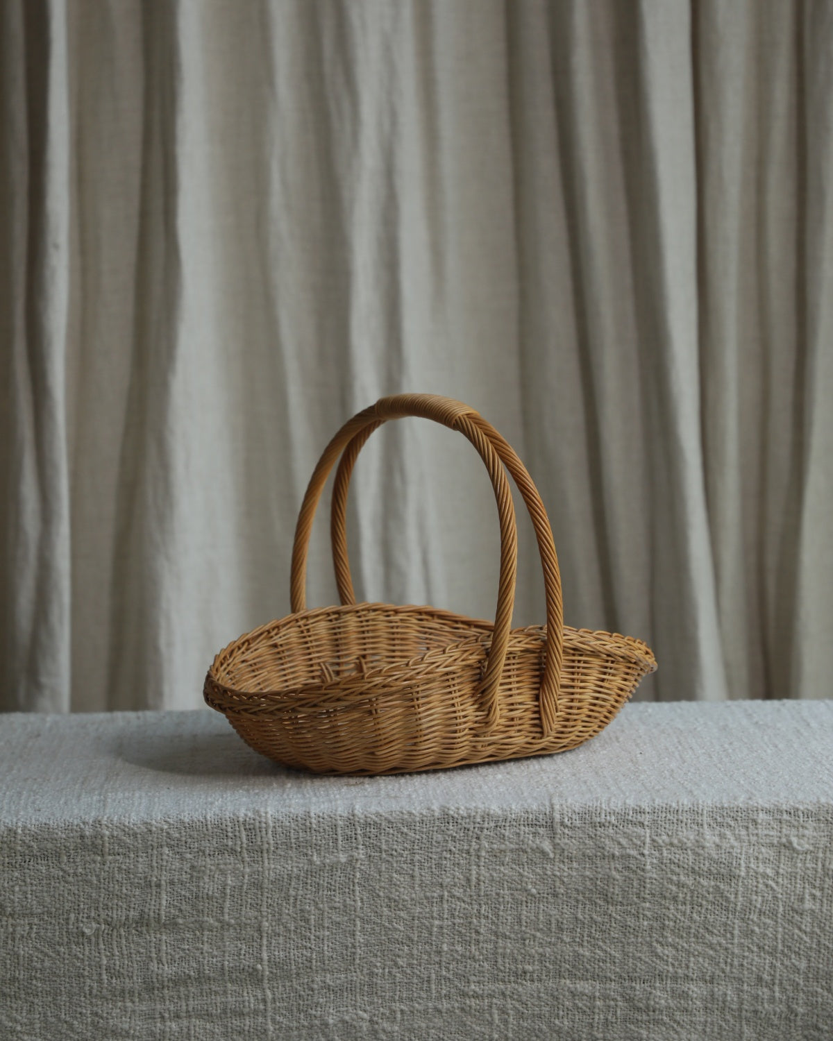 Natural rattan Venus gathering basket with tall handle on linen-covered table