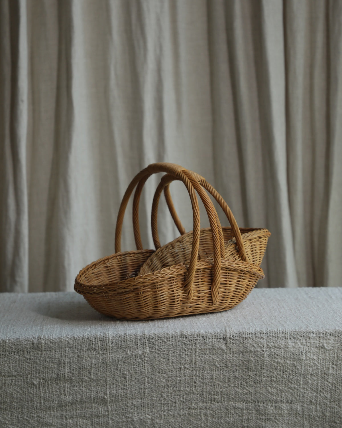 Natural rattan Venus Gathering Basket with curved handles on a linen-covered table