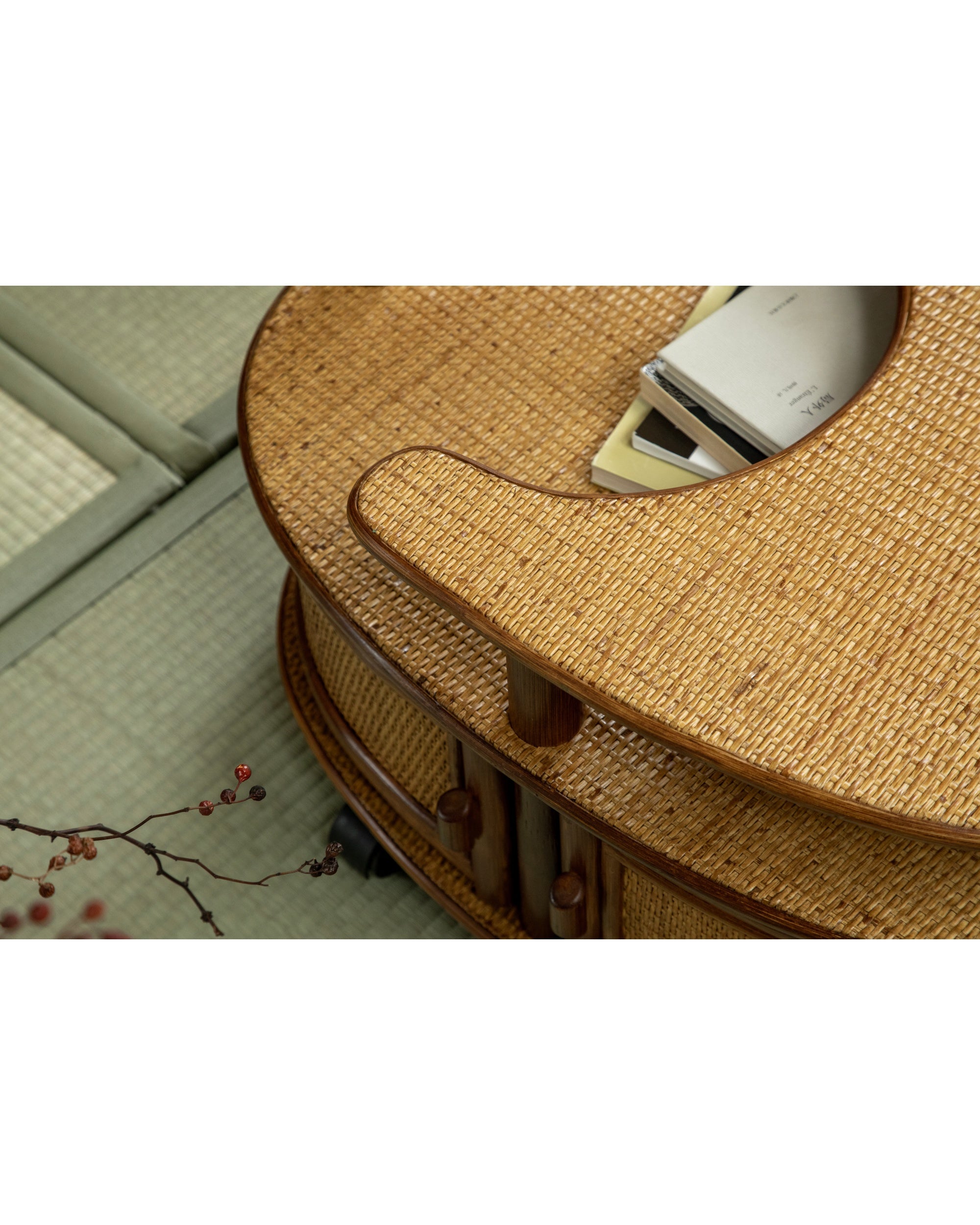 Noa Rattan Wheeled Table, natural woven Manau cane side table with wooden trim and recessed top holding books.