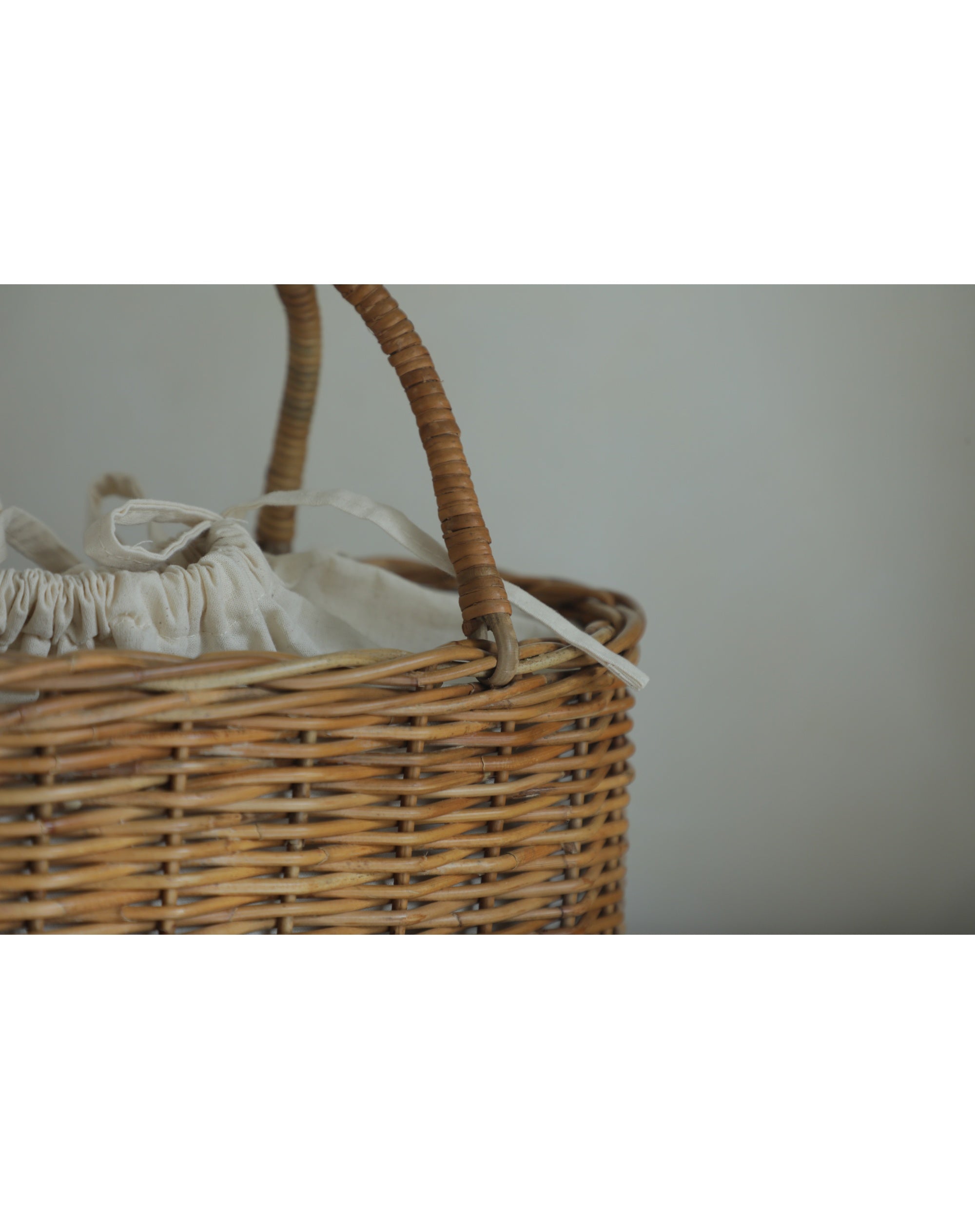 Natural rattan handbag with woven basket body, curved handle, and fabric drawstring lining