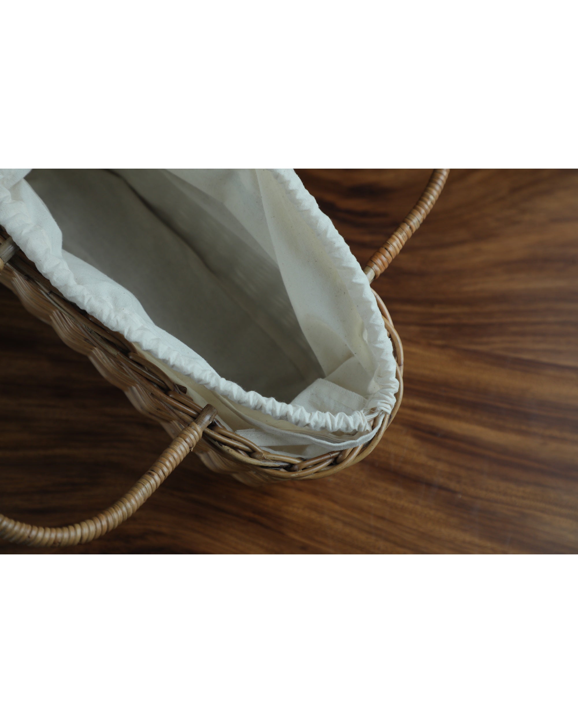Handwoven rattan handbag with cream lining and curved handles on a wooden surface