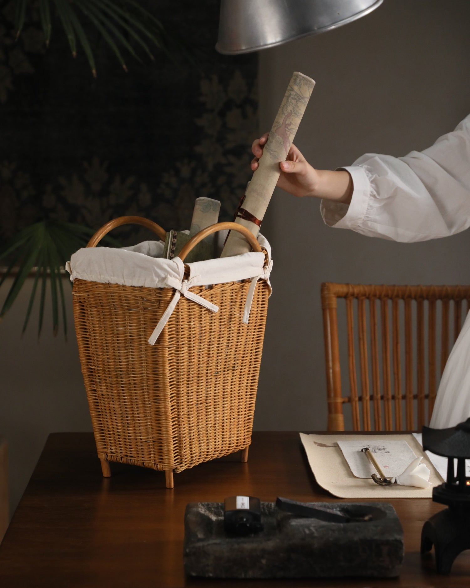 Luna Storage Basket: Woven rattan basket with cotton lining, holding a scroll.