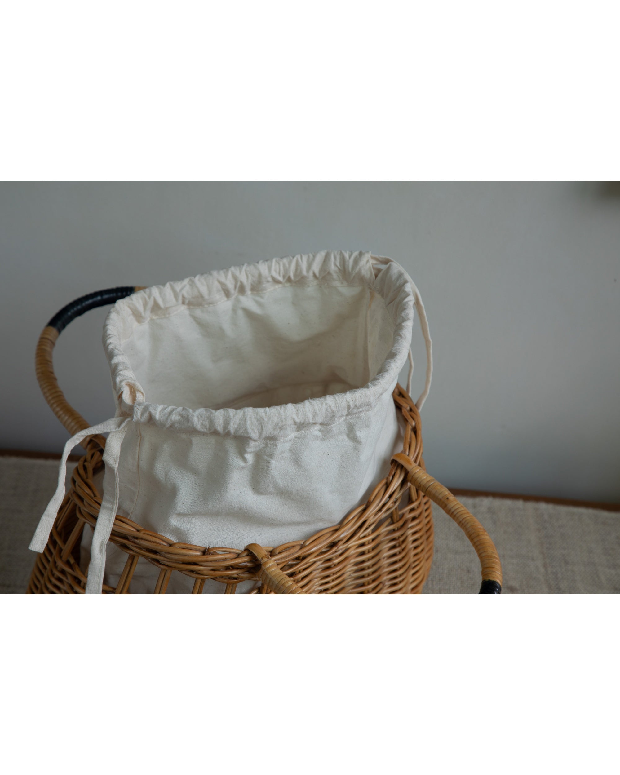 Ivy Hand Bag made of natural woven rattan, featuring a drawstring fabric liner and handles.