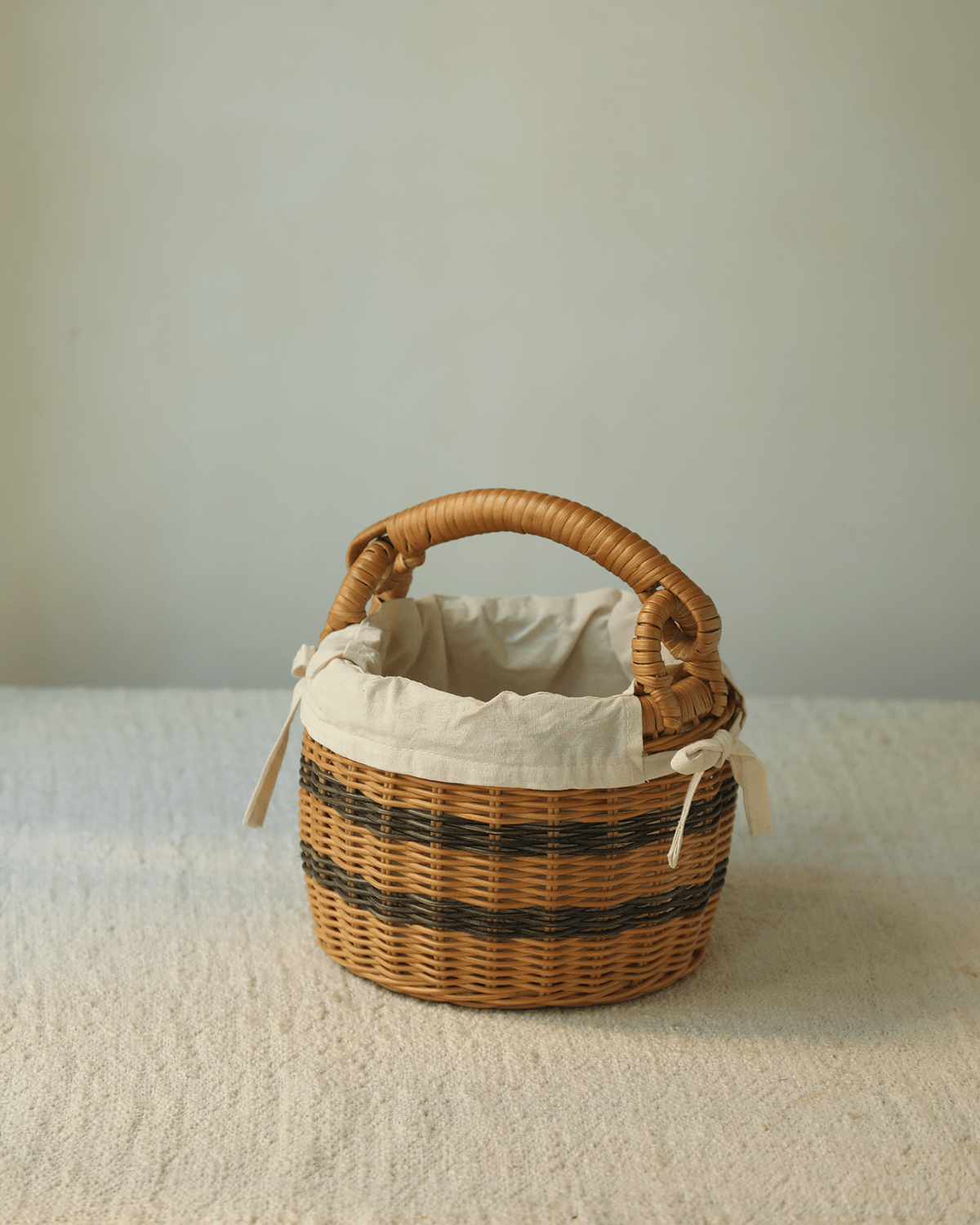 Handwoven rattan bucket basket with dark brown stripes, natural handle, and cotton liner.