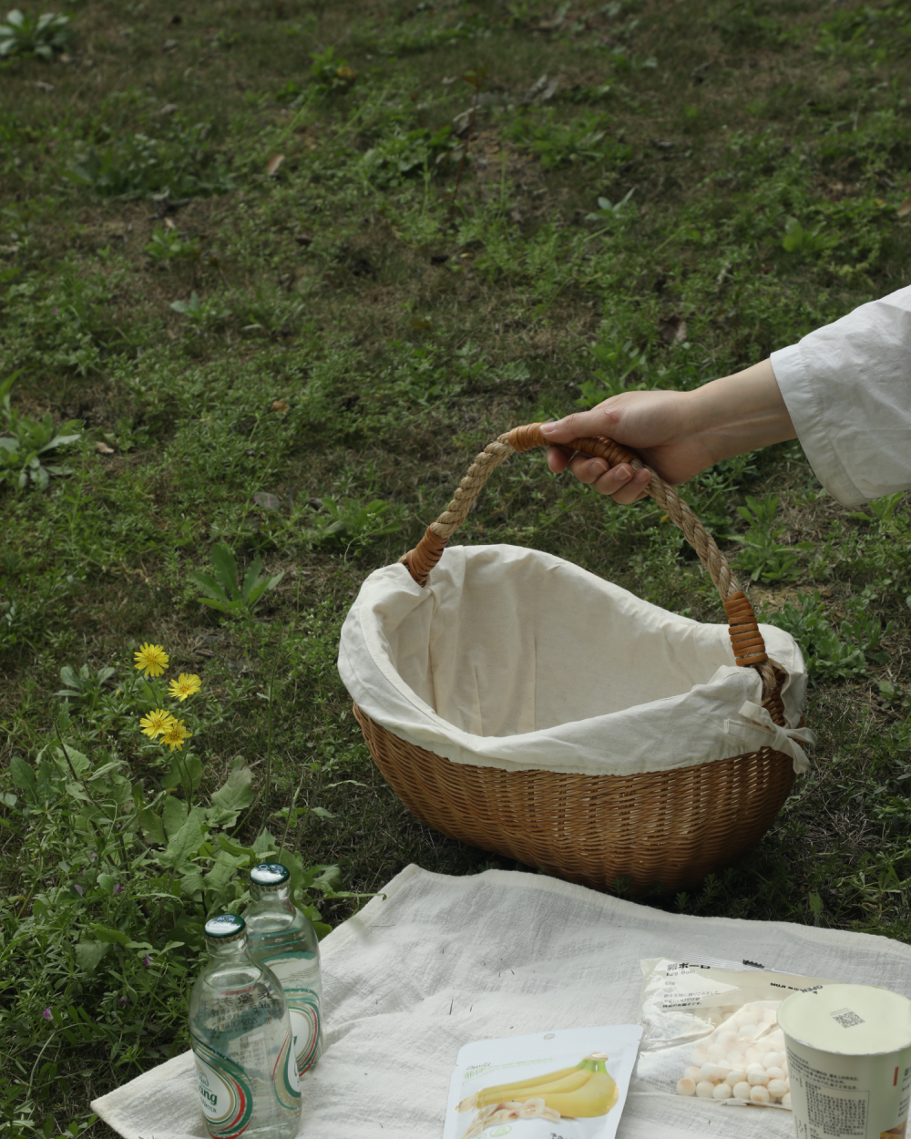 Hand carrying a woven storage basket with white cloth lining on grass, Aurelia Basket