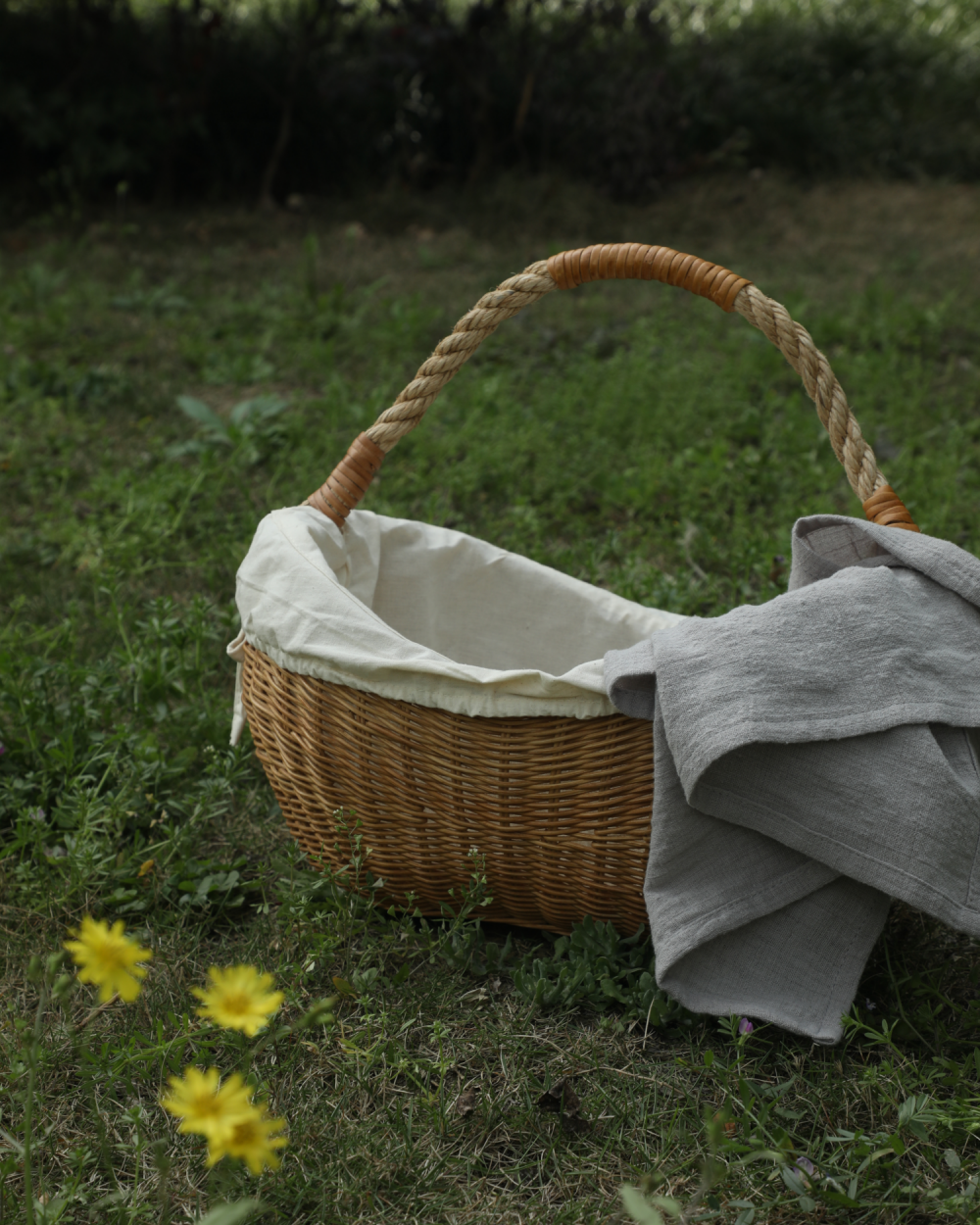 Handwoven wicker storage basket with rope handle and removable lining on grass