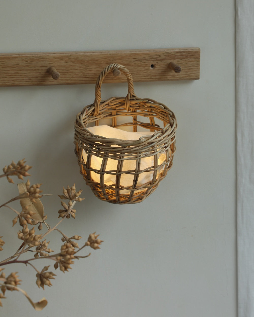 Woven rattan Cove hanging basket, deep structure, artisanal arched handle, warm glow inside.