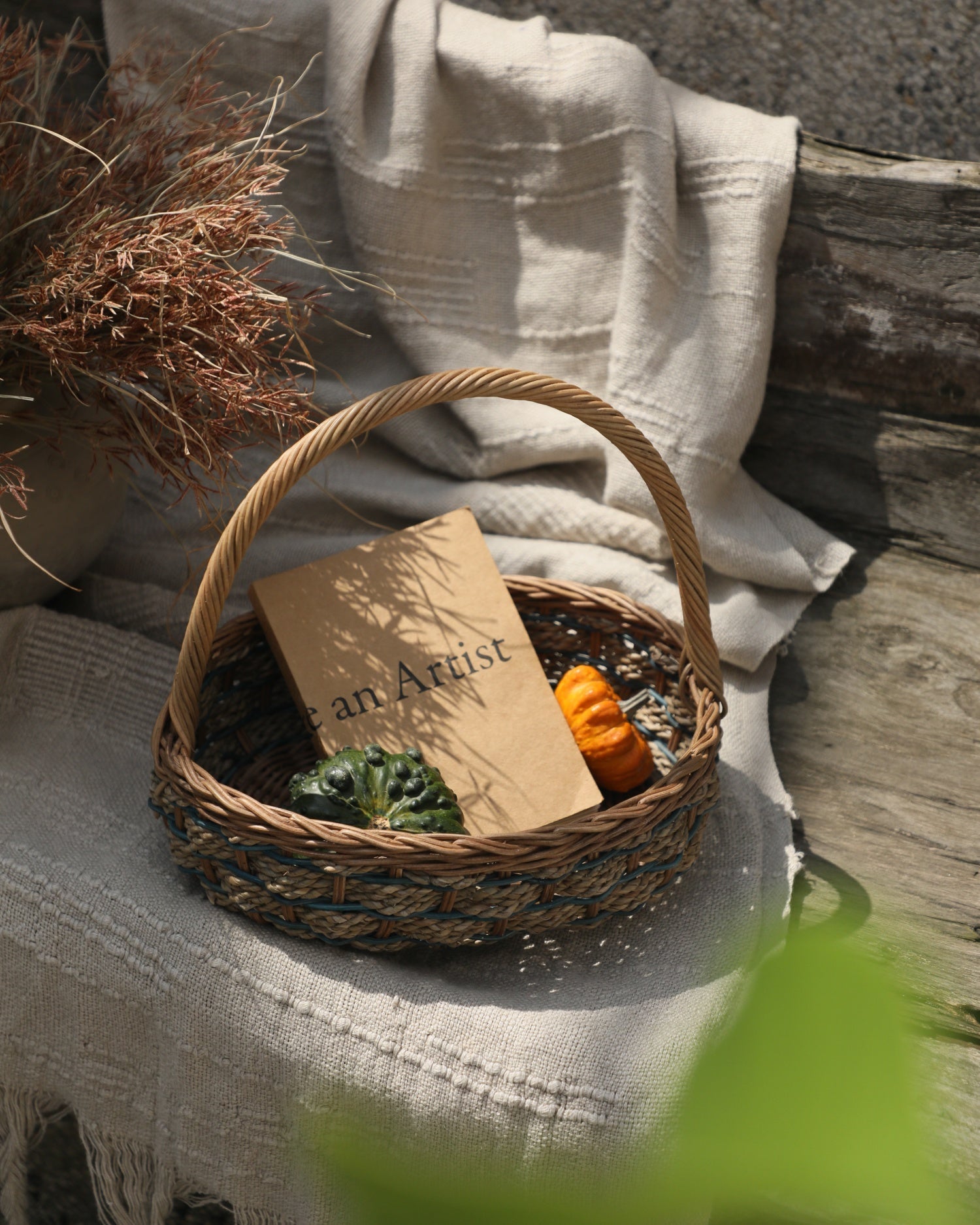 Viney Tote Basket with handles, woven rattan, holding book and decorative gourds.