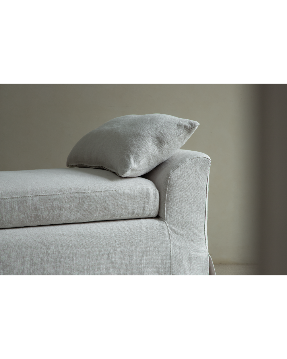 Close-up of the Alina Bench upholstered in textured linen gray fabric with a cushion.