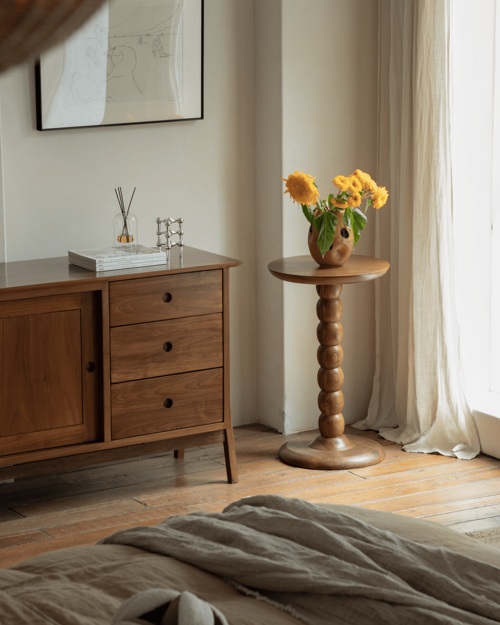 Compact Nerida teak side table with stacked bead design and round top, holding yellow flowers.