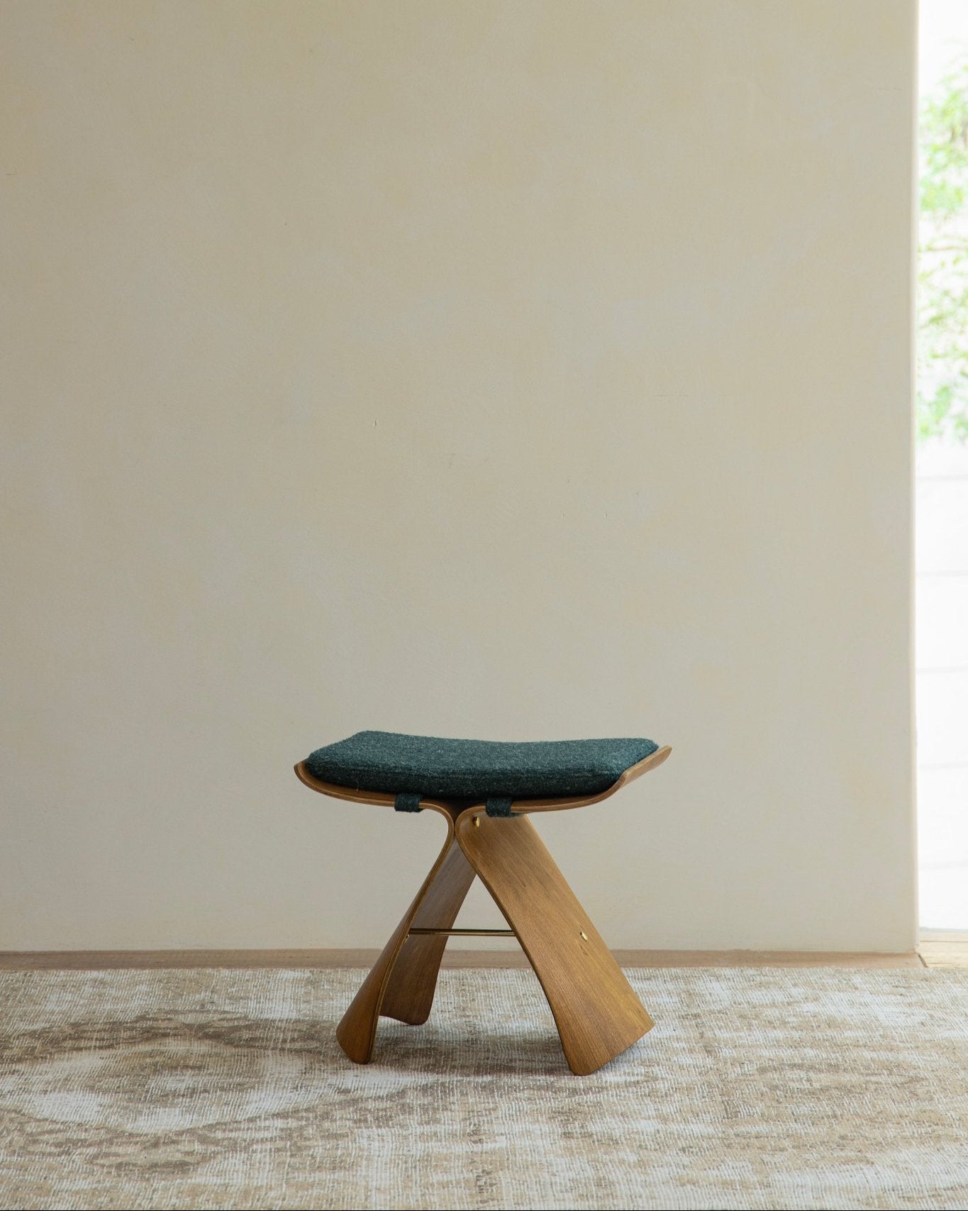 Butterfly Stool in natural wood with green cushion, classic modern design, solid bent wood construction, elegant seating.