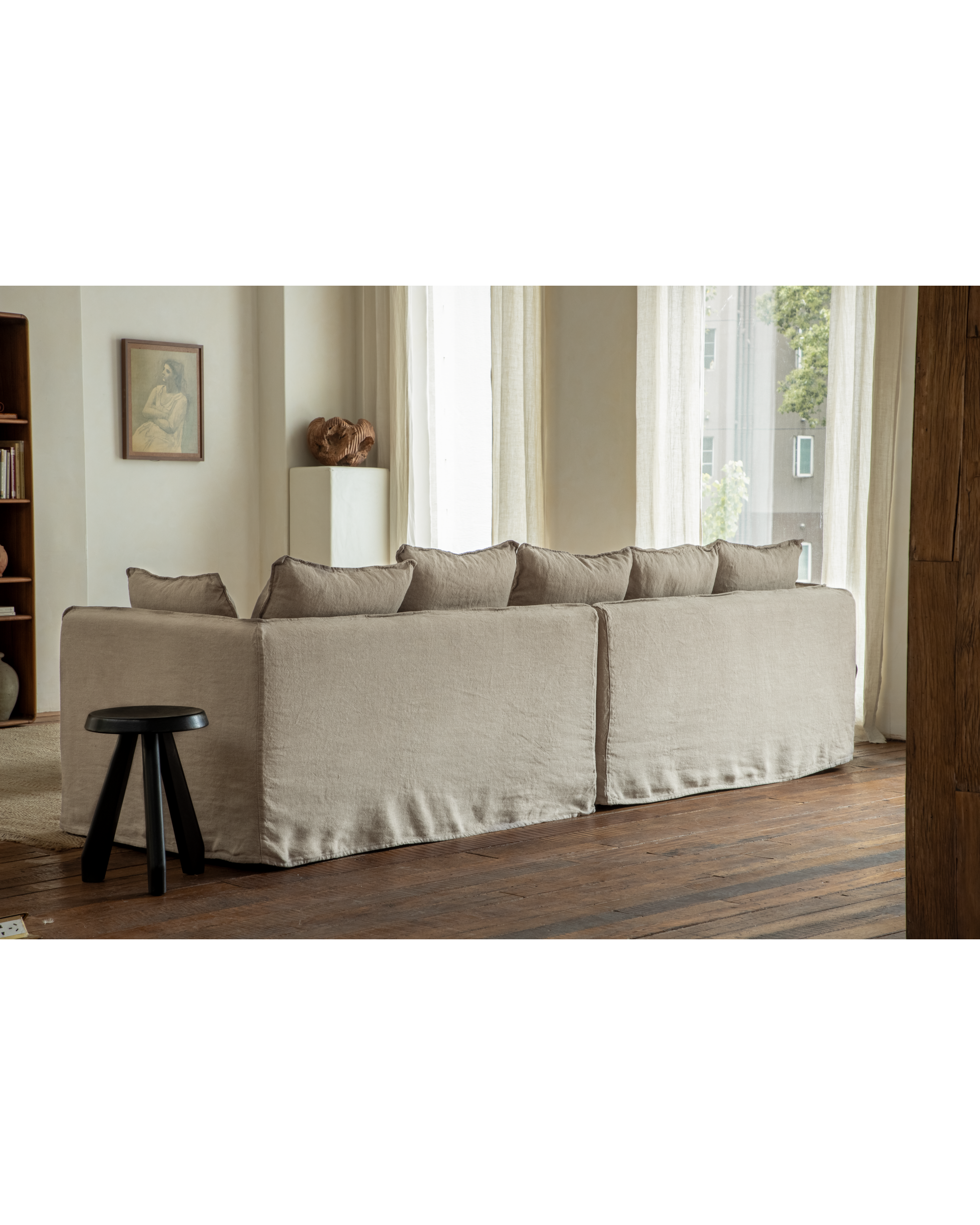 Back view of the Camille sectional sofa in khaki linen, featuring plush cushions and a nearby black stool.