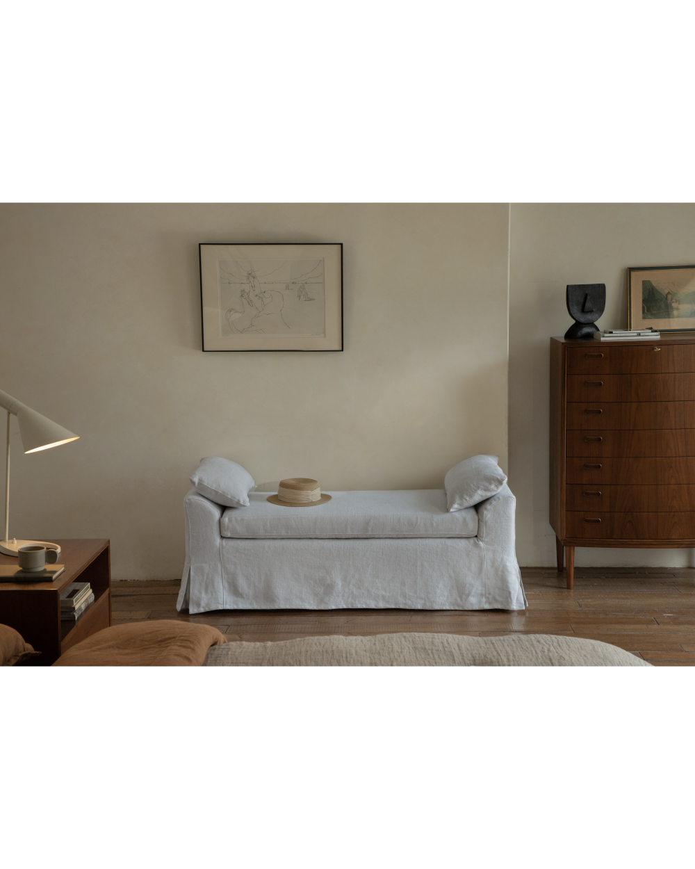 Elegant light grey linen Alina bench with slipcover, styled with straw hat in a bedroom.