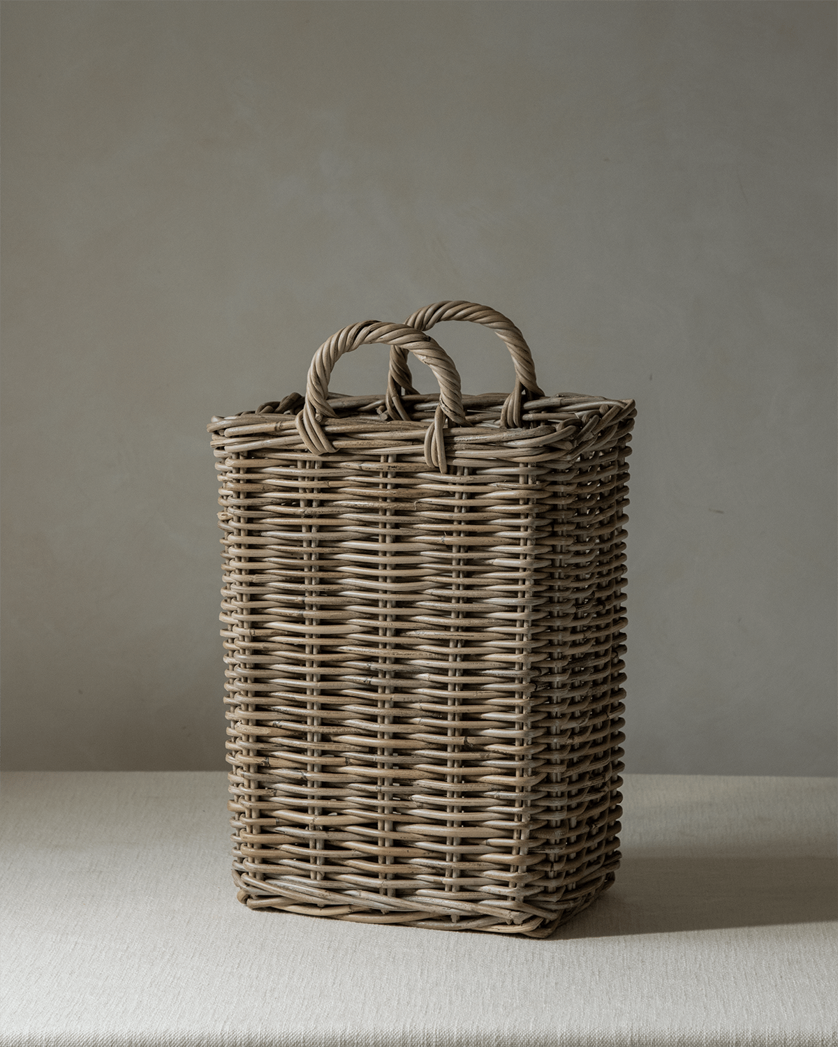 Oliver Basket: Tall, narrow, handwoven natural rattan storage basket with braided handles.