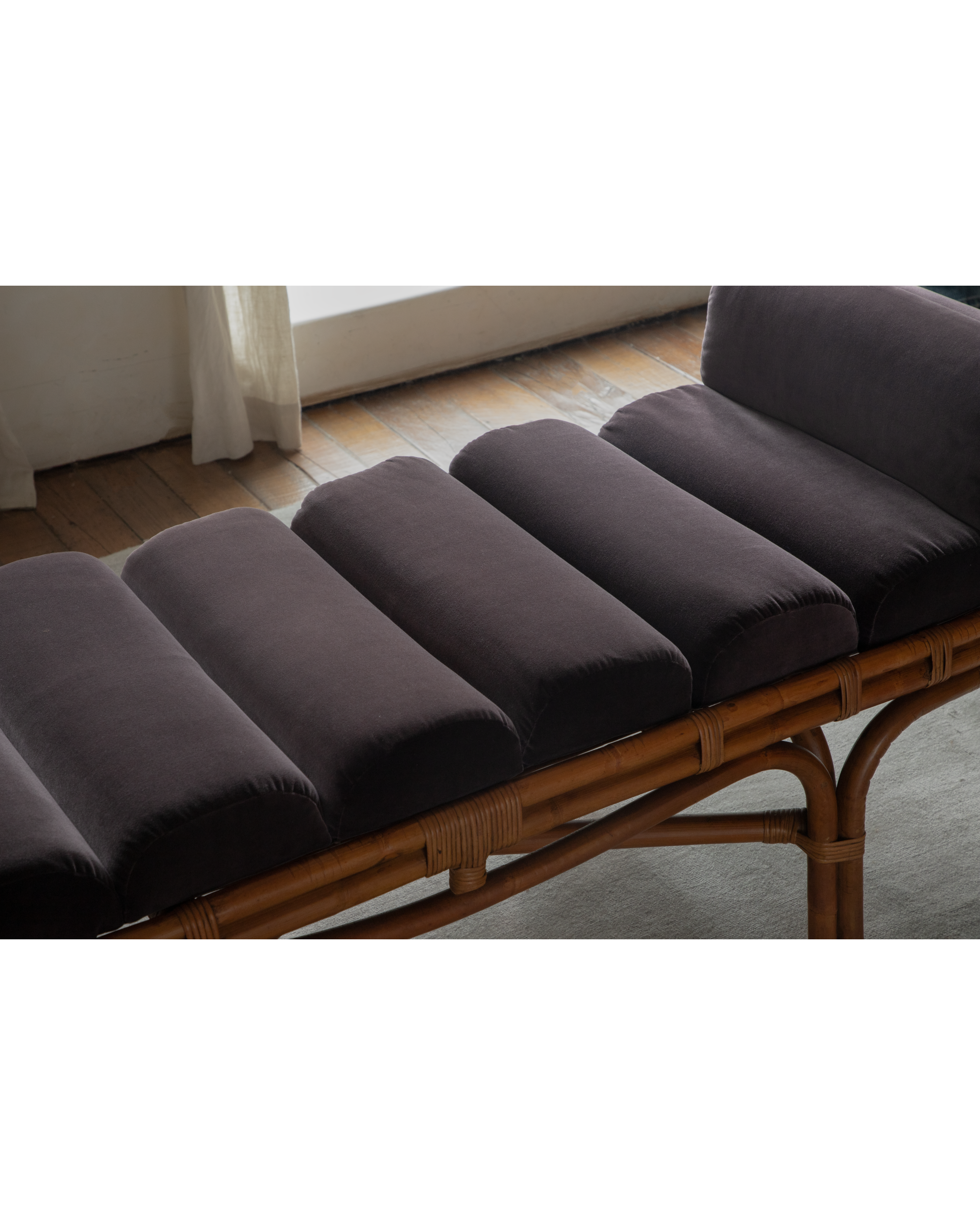 Detailed view of Bridget Bench featuring segmented dark velvet cushions and woven rattan frame.