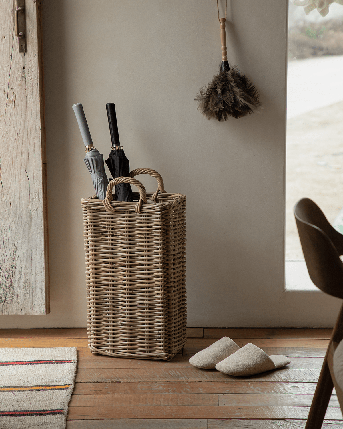 Oliver Basket: Handwoven rattan storage basket with handles, holding umbrellas. Natural & versatile.