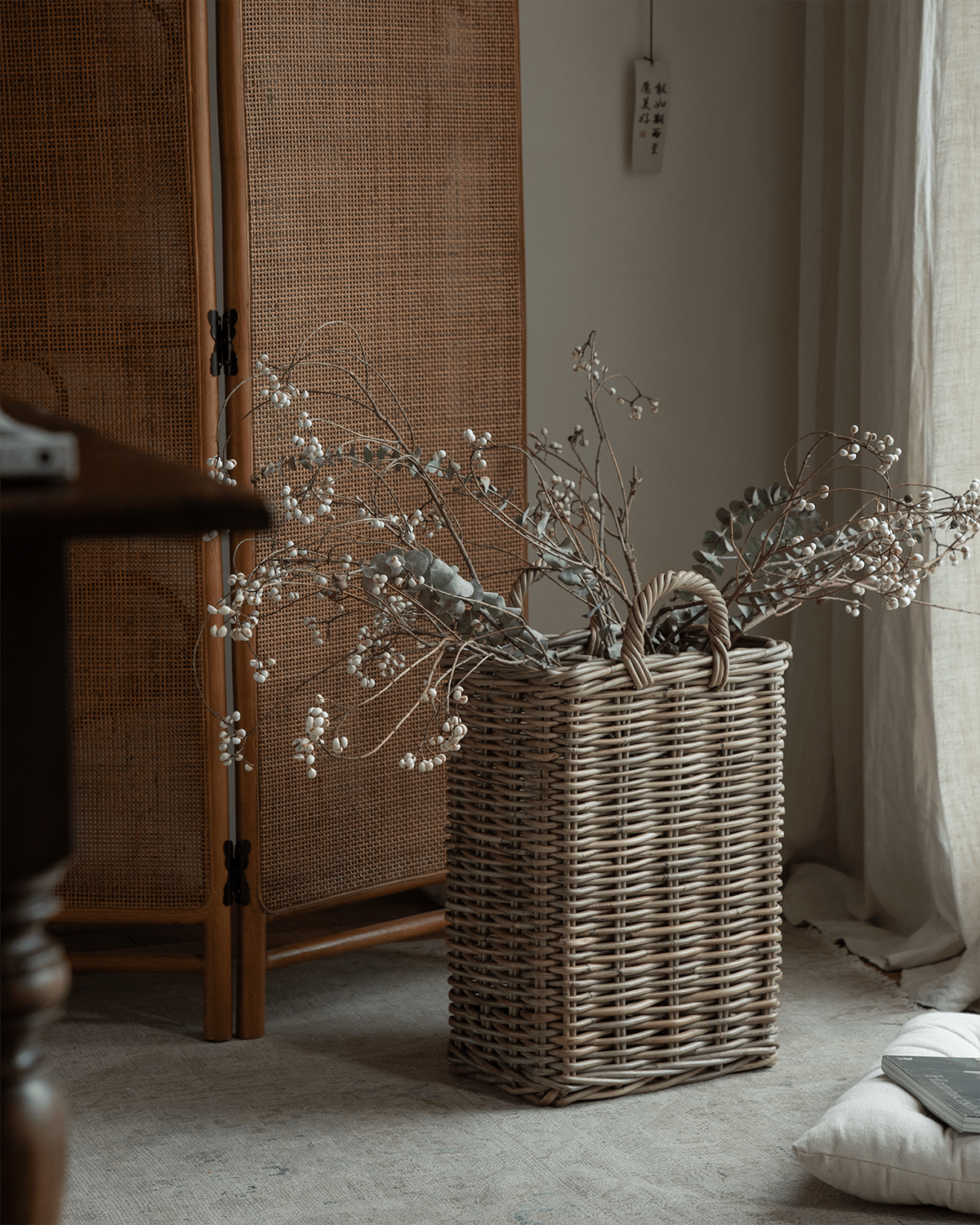 Oliver Basket: Tall, handwoven natural rattan storage basket with dried white berry branches.