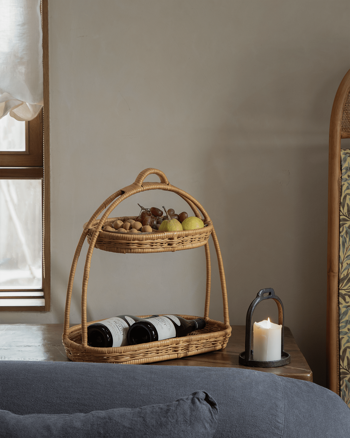 Natural rattan two-tier Beatrice Stand holding fruits and wine bottles