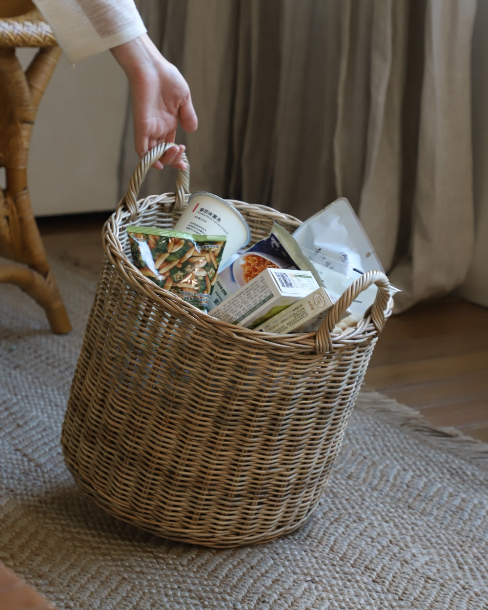 Aria round woven rattan storage basket with handles, filled with items.