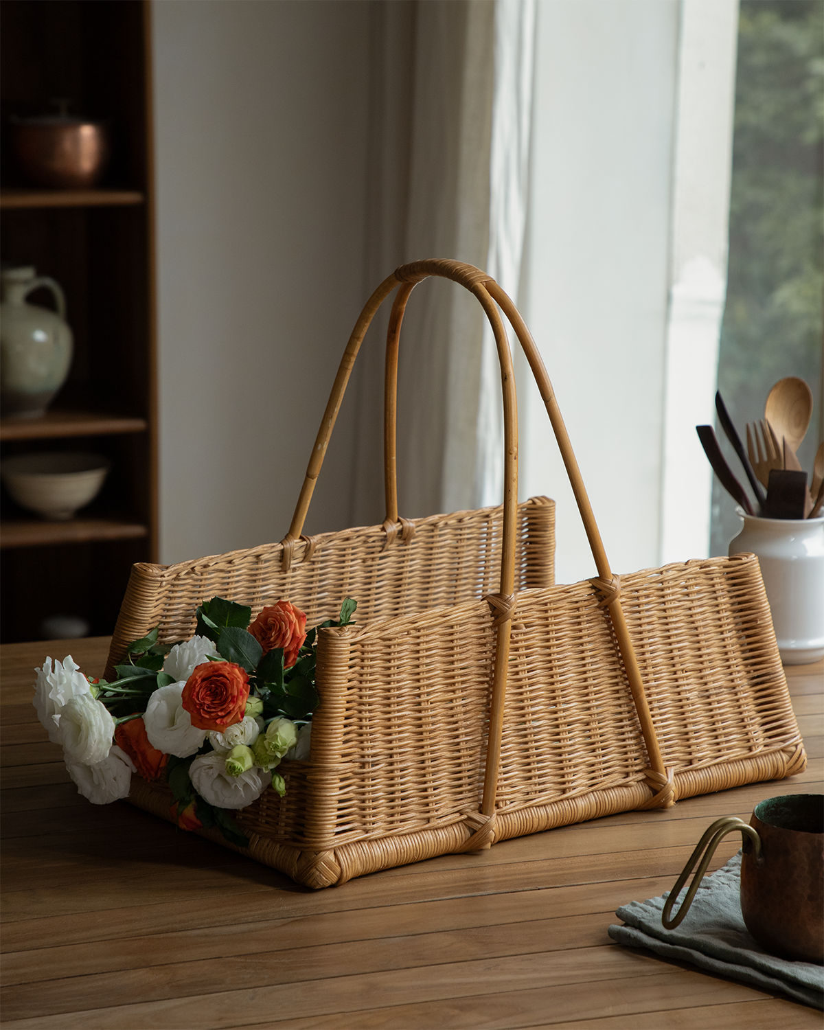 June Basket: hand-woven natural rattan with unique concave shape and double handles, displaying flowers.