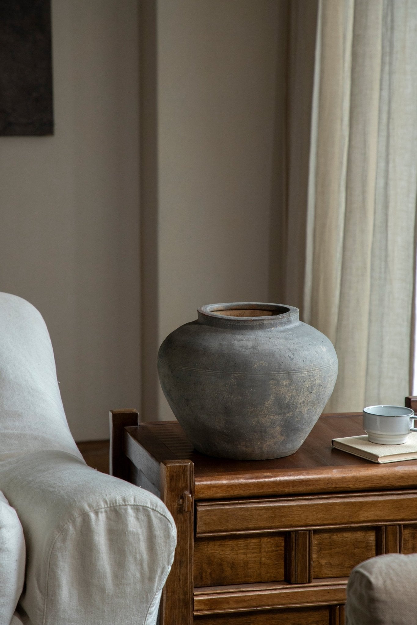Vintage clay pot on a wooden table with a teacup. Neutral home decor accent. Clay material.