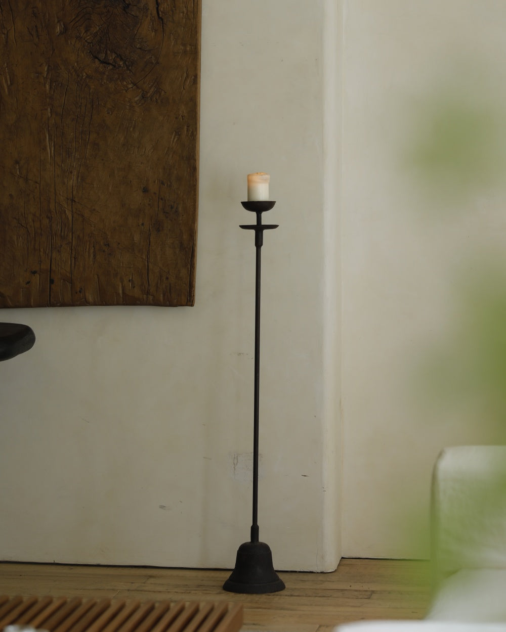 Black iron floor candlestick with bell base, holding lit candle.