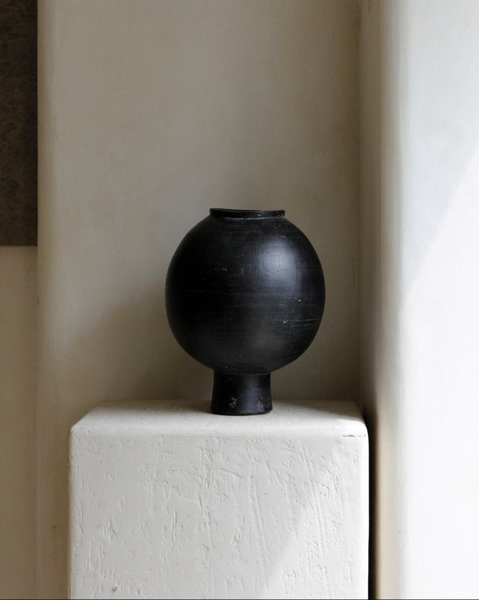 Black ceramic sphere vase on a white block, minimalist home decor