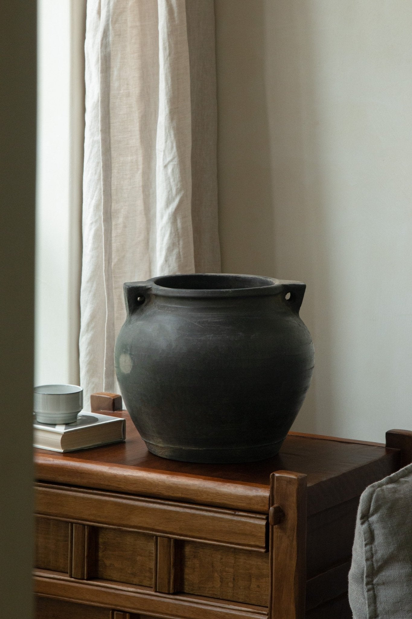 Large vintage clay pot with handles, neutral decor accent, on wooden surface with teacup and book.
