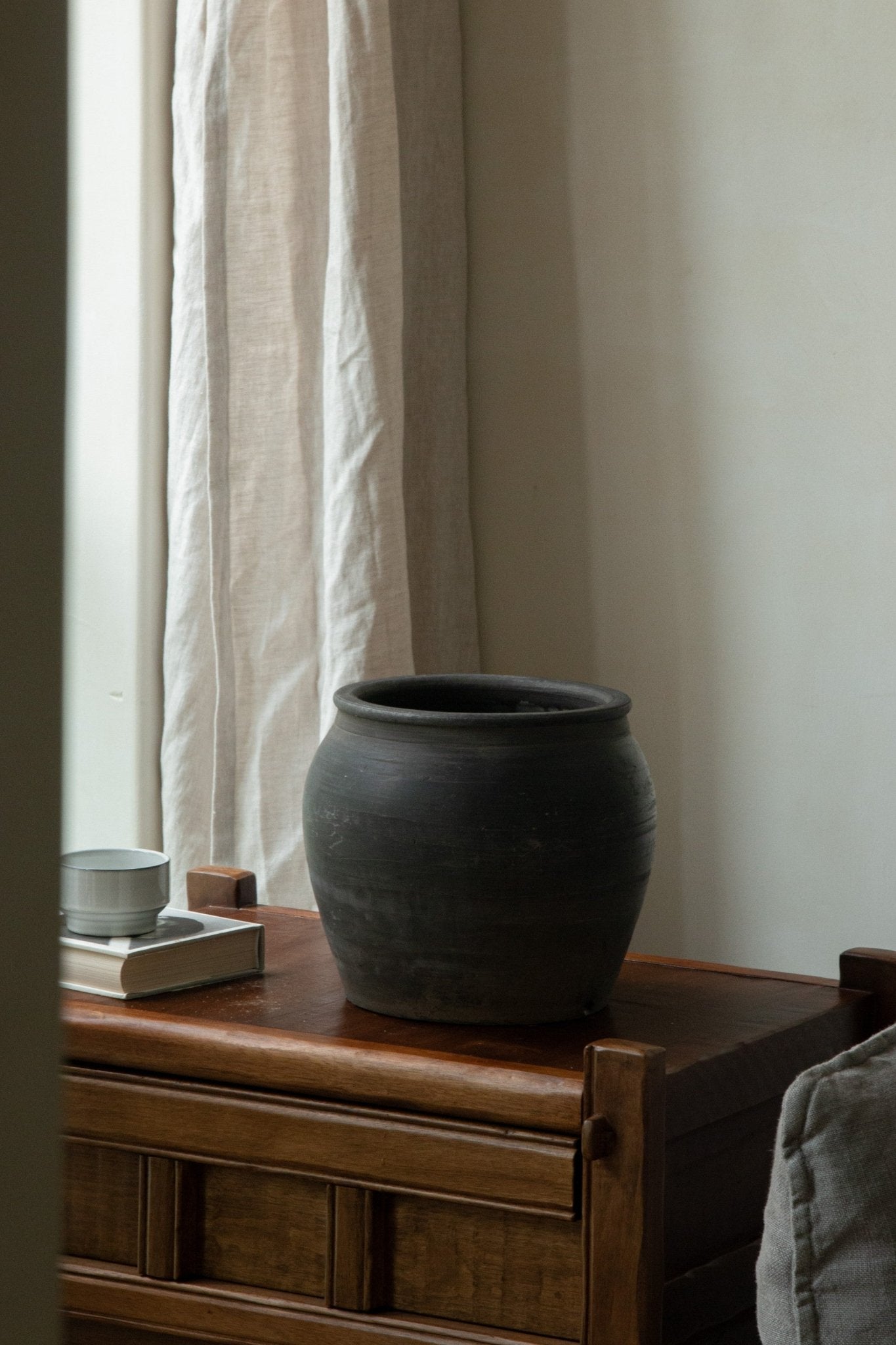 Large black clay pot on wooden chest, neutral home decor, clay material, product detail.