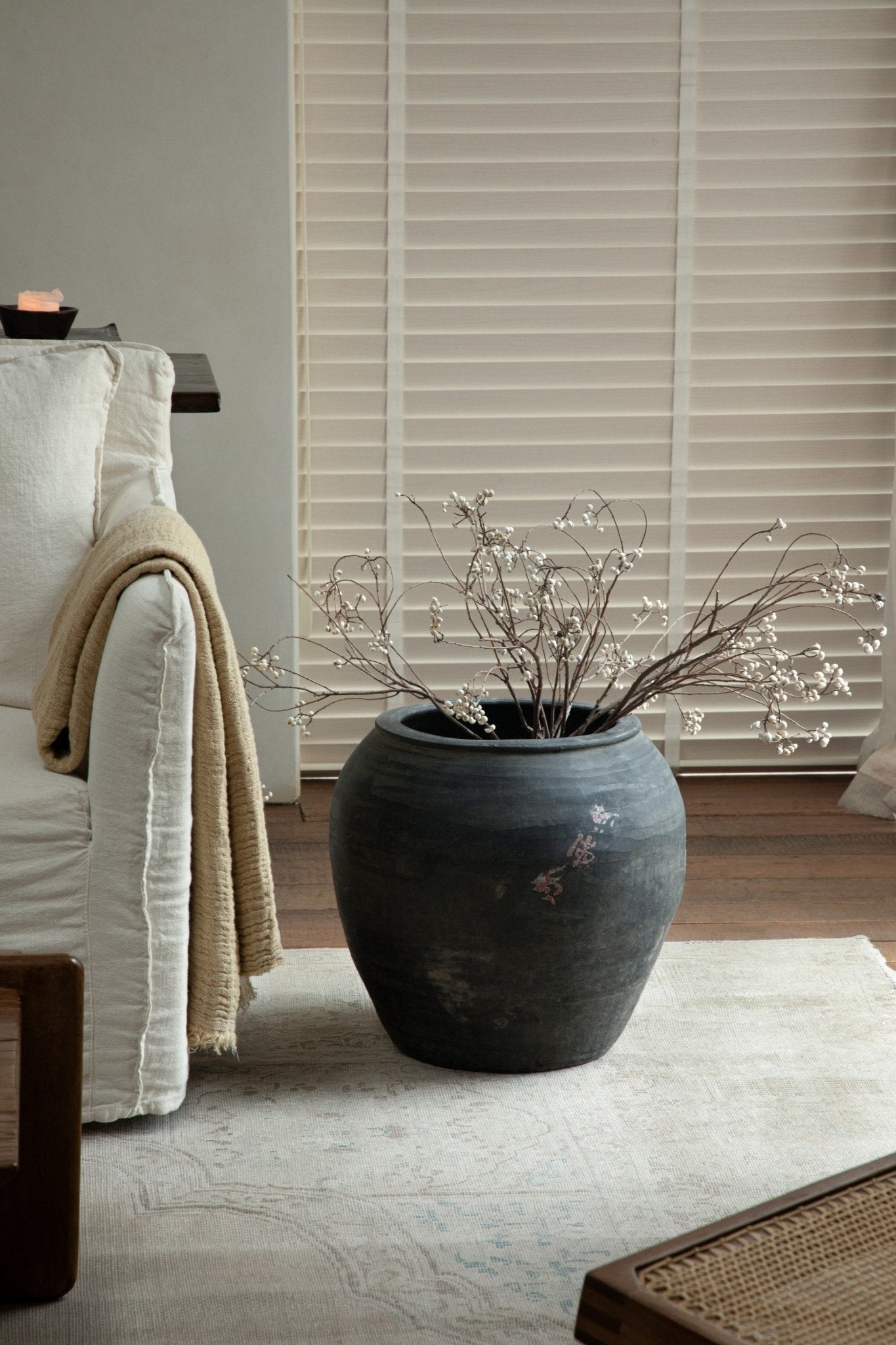 Large clay pot, neutral gray, home decor accent with branches, on a wooden table. Clay material.