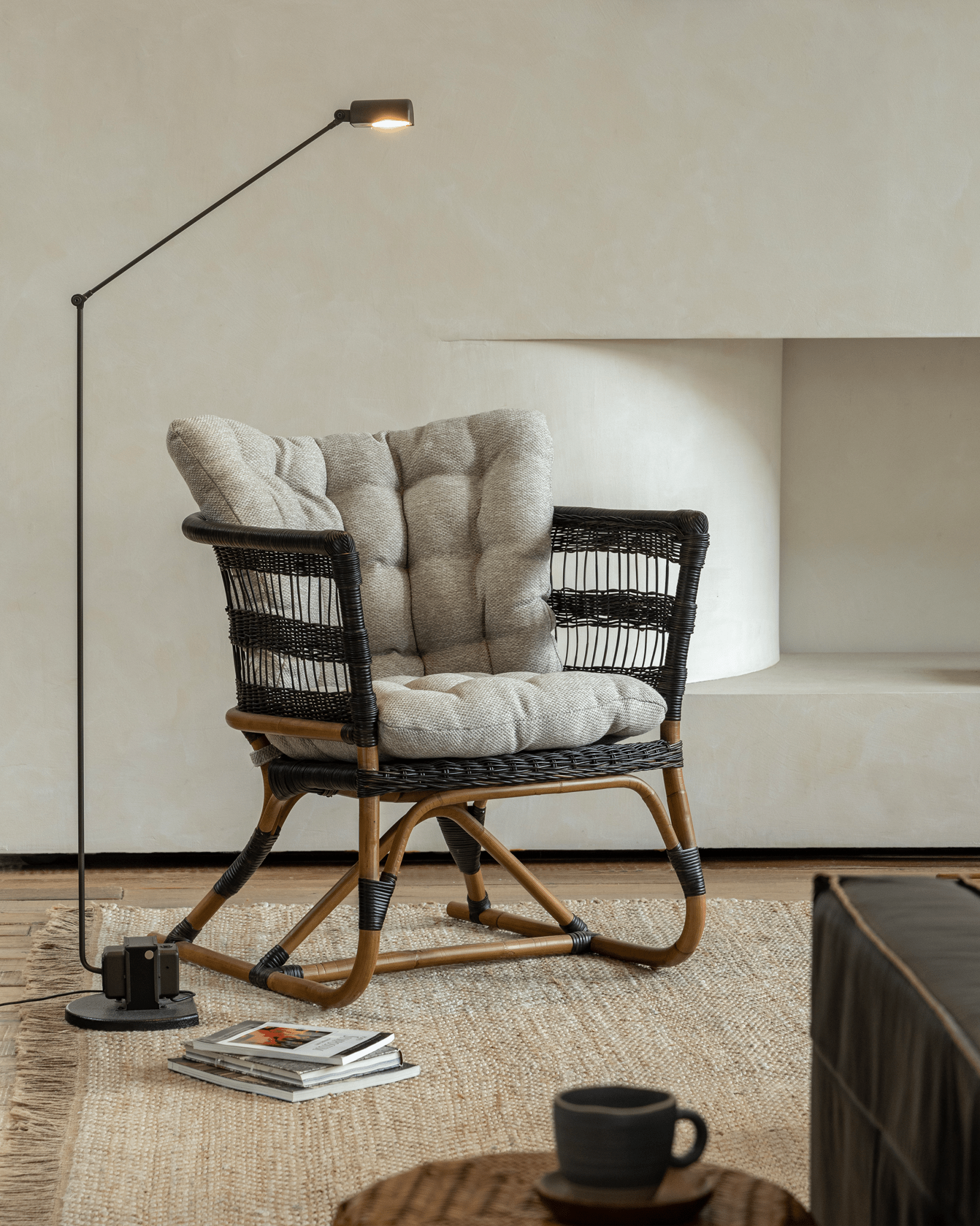 Helian Rattan Chair with gray cushion, natural rattan frame and black accents, in a cozy interior setting