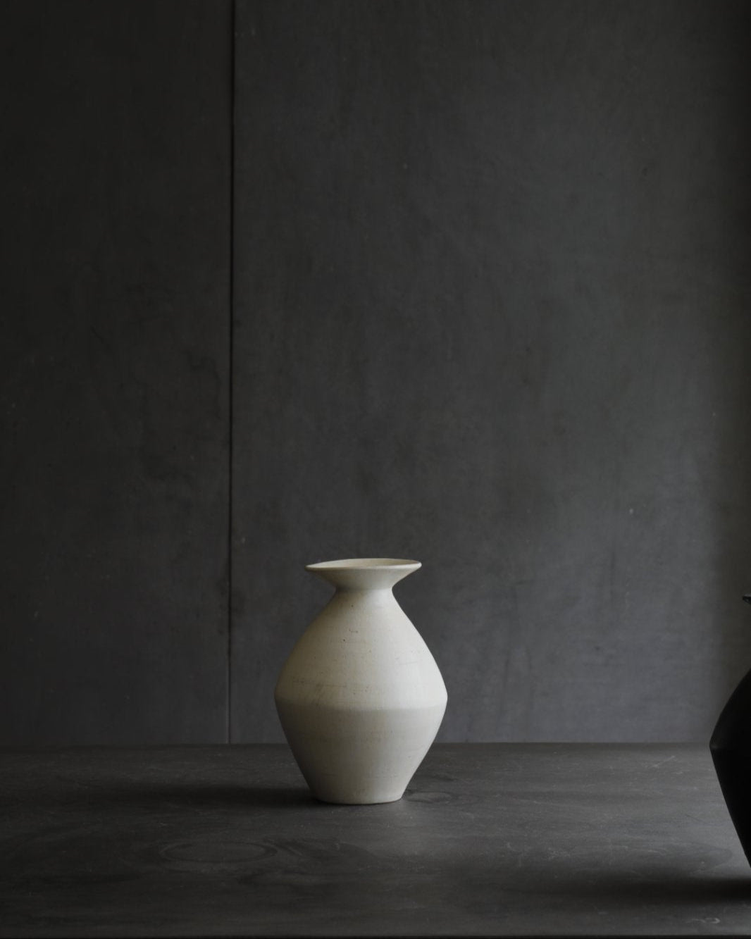 Off-white ceramic vase on dark surface. Modern home decor.
