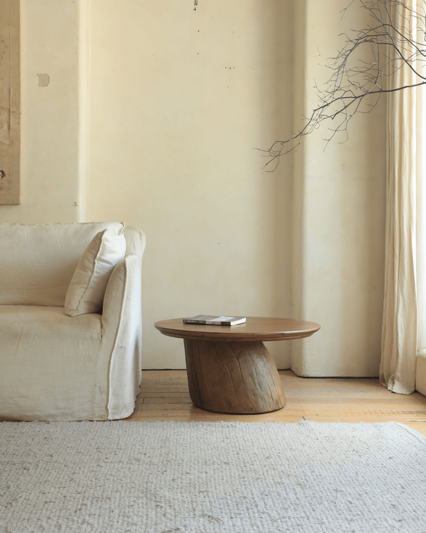 Alva Side Table in a living room setting, featuring natural wood, distorted base, and a book, modern interior.