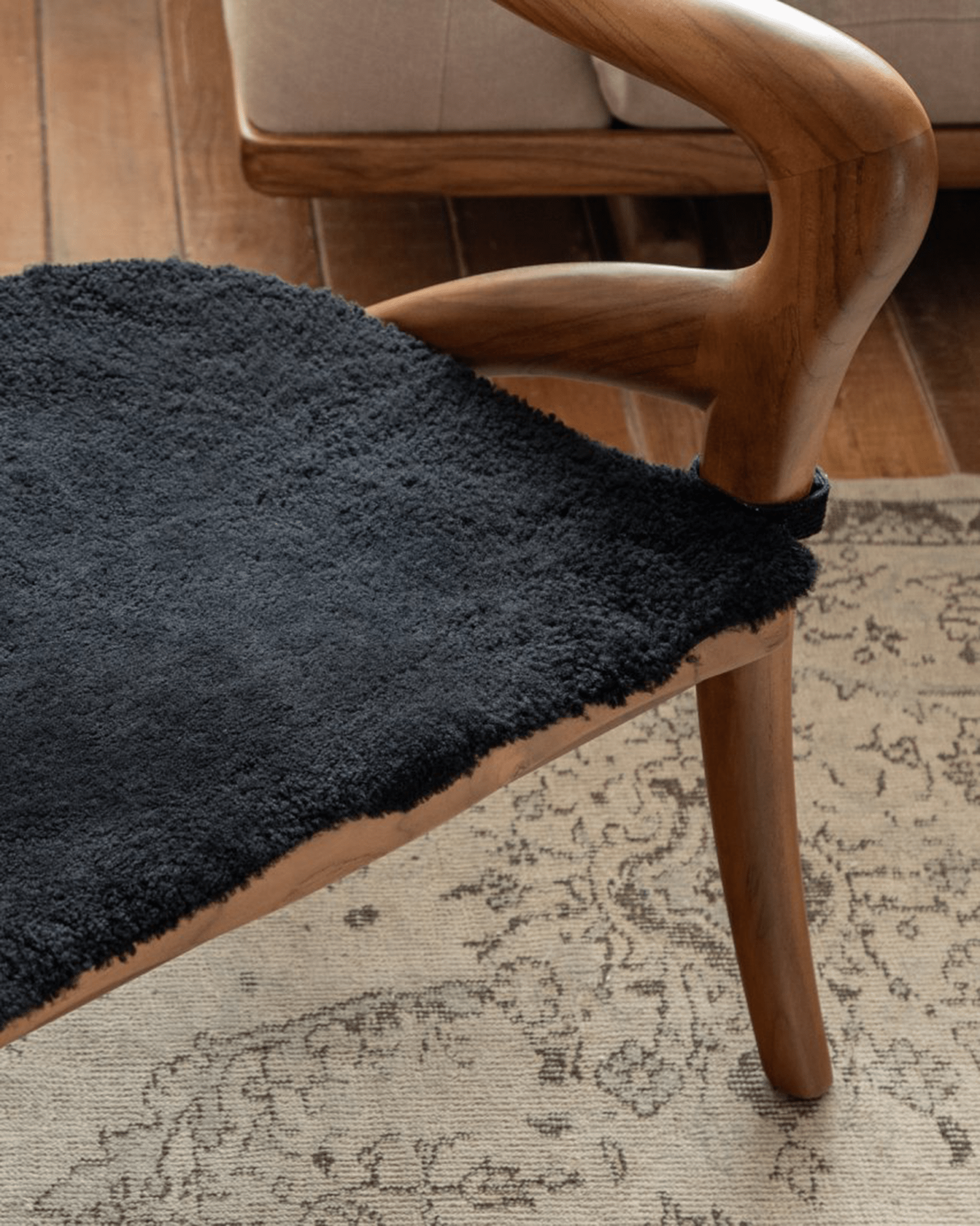 Olivia Chair detail: Black textured seat cushion on teak wood frame, modern design, curved backrest.