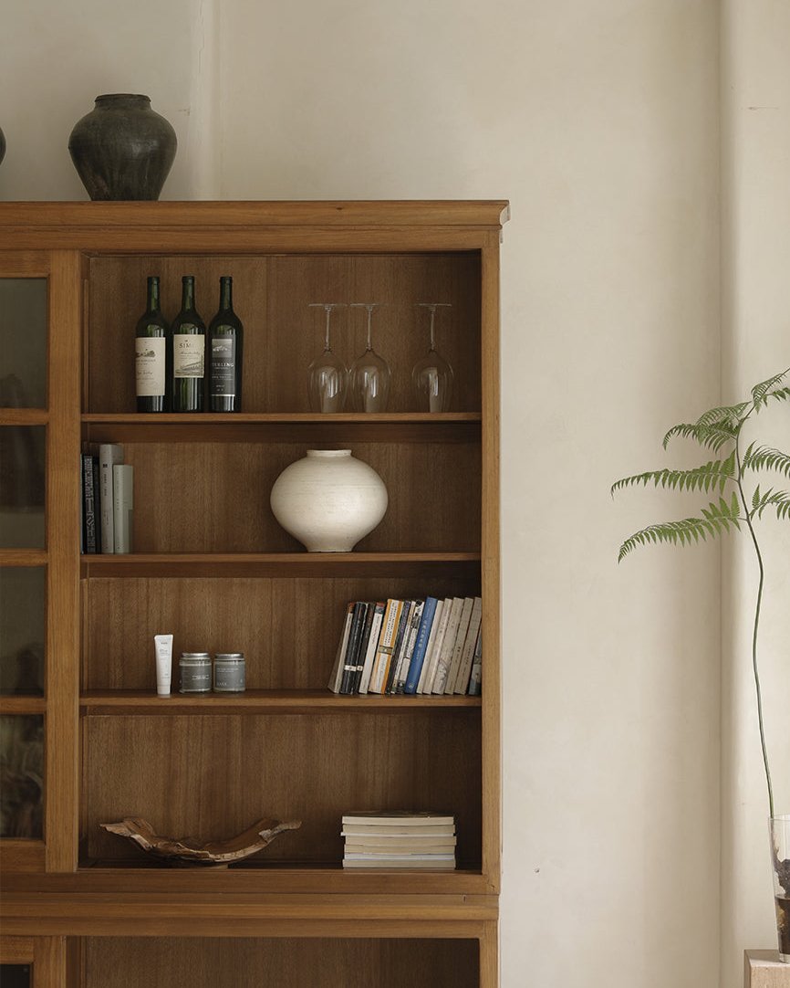 African teak glass bookcase with display of wine bottles, glasses, and books