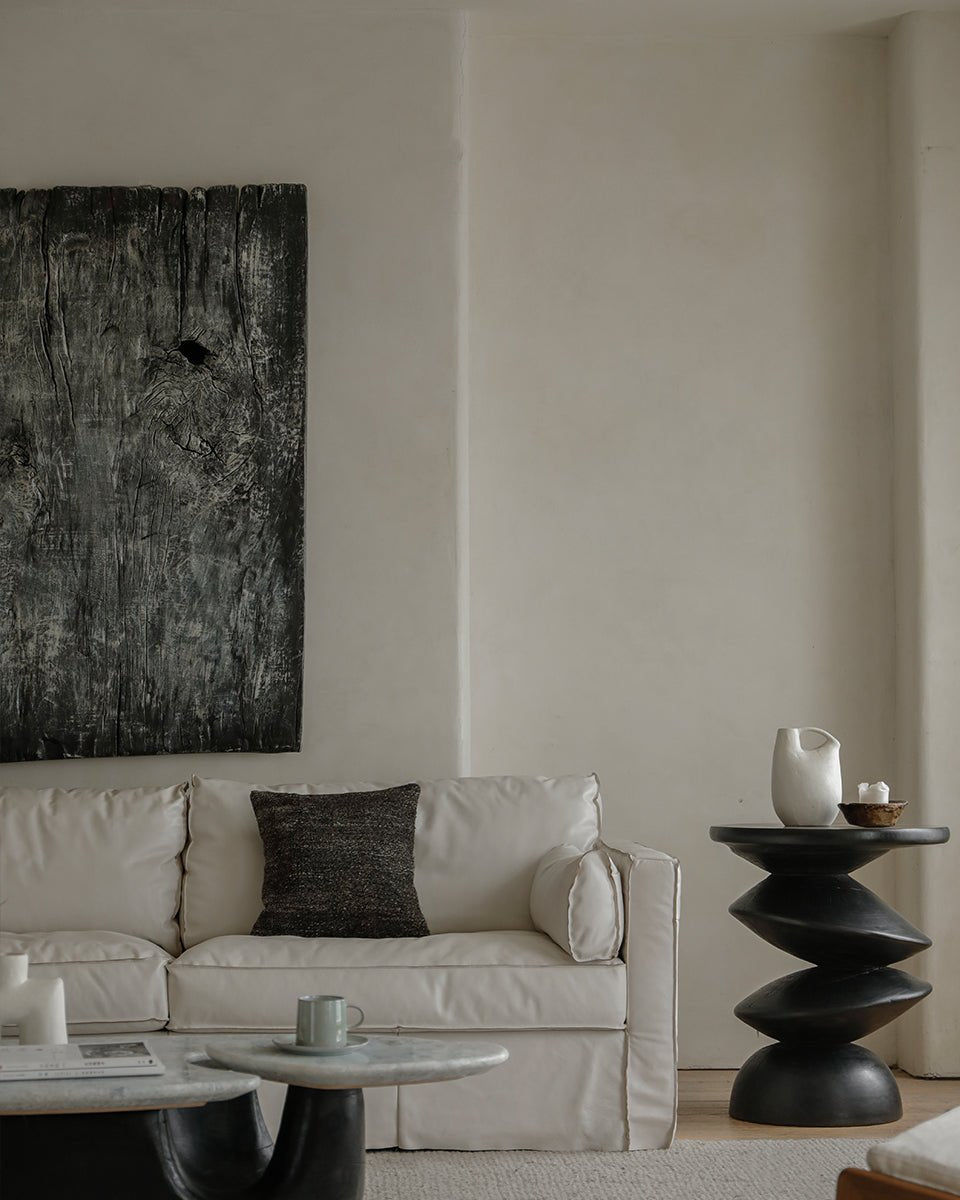 White skirt leather sofa in a modern living room, with a sculptural side table and dark wood art, creating an elegant space.