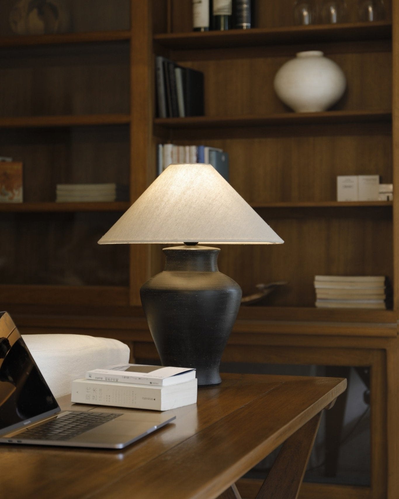 Short neck lamp with clay base, linen shade, and modern design on wooden table, MacBook next to it